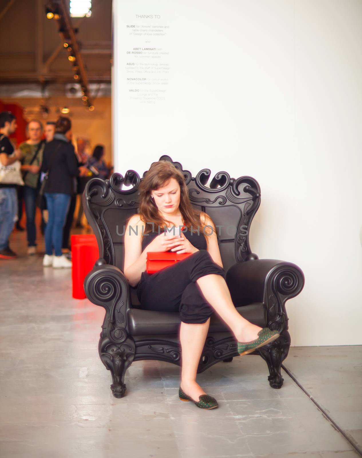 MILAN, ITALY - APRIL 16: Pretty young businesswoman reading message on smartphone while sitting at sofa during the Fuorisalone, Milan Design week at Tortona space location on April 16, 2015