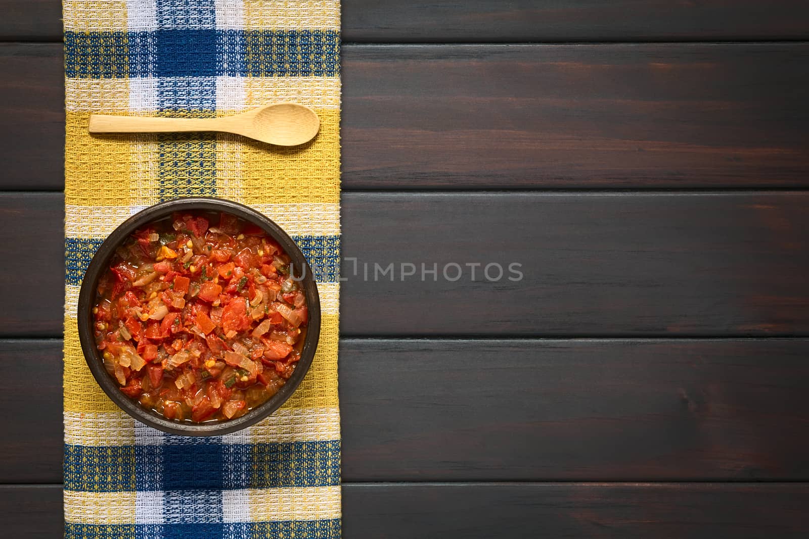 Overhead shot of Colombian hogao or criollo sauce (salsa criolla) made of cooked onion and tomato, served as accompaniment to traditional dishes. Photographed on dark wood with natural light.
