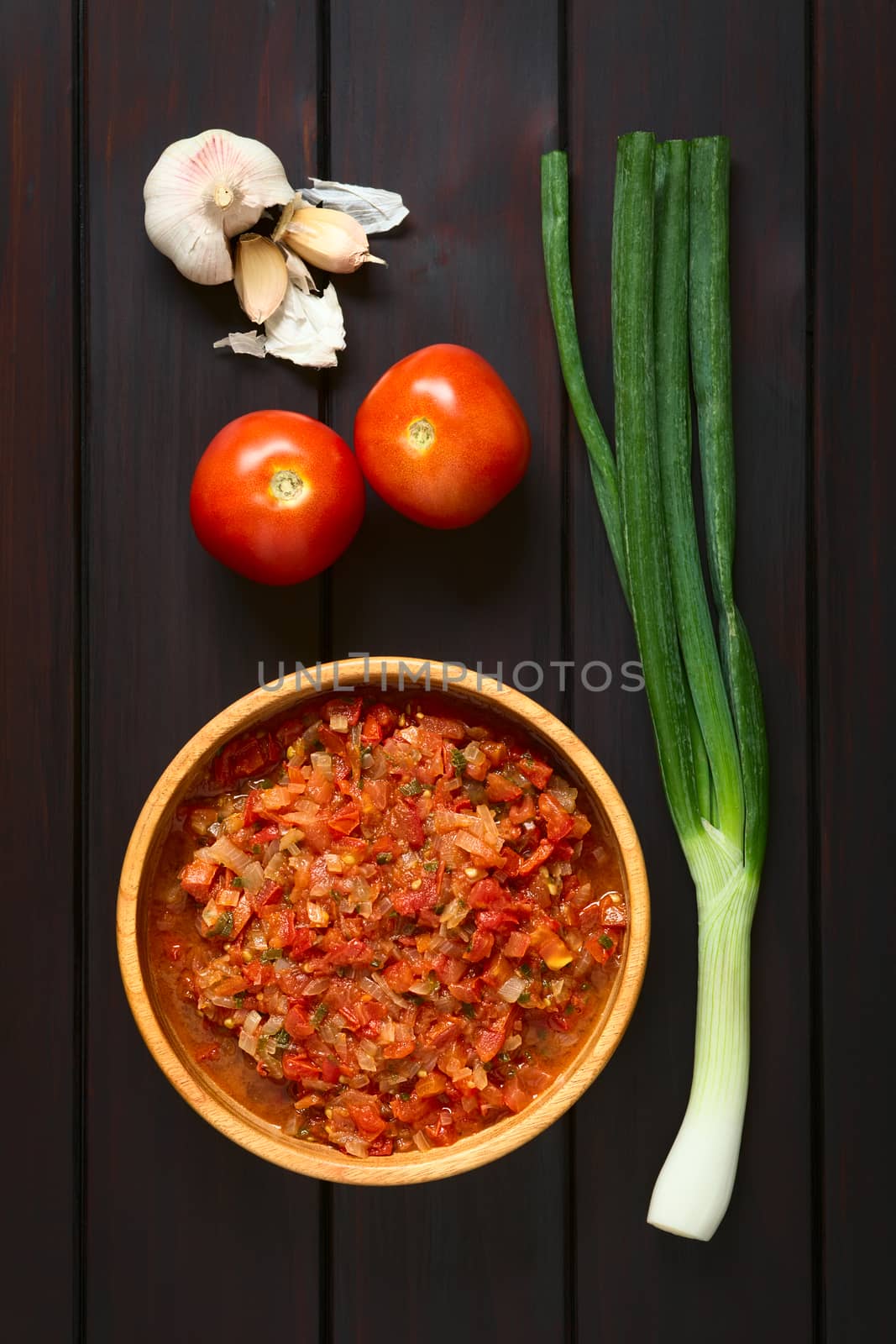 Overhead shot of Colombian hogao or criollo sauce (salsa criolla) made of cooked onion and tomato, served as accompaniment to traditional dishes. Photographed on dark wood with natural light.