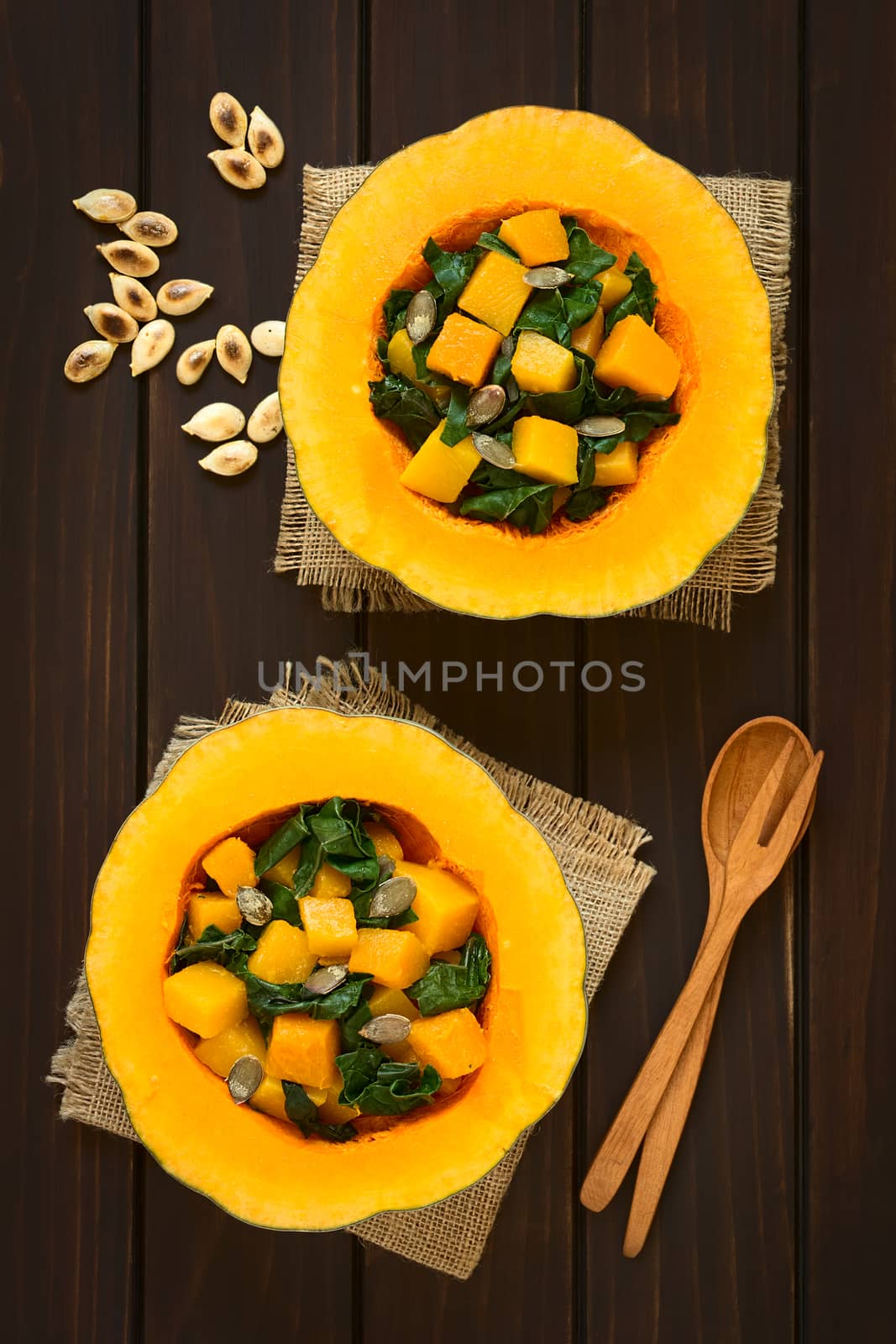 Pumpkin and chard salad with roasted pumpkin seeds served in pumpkin halves, photographed overhead on dark wood with natural light  
