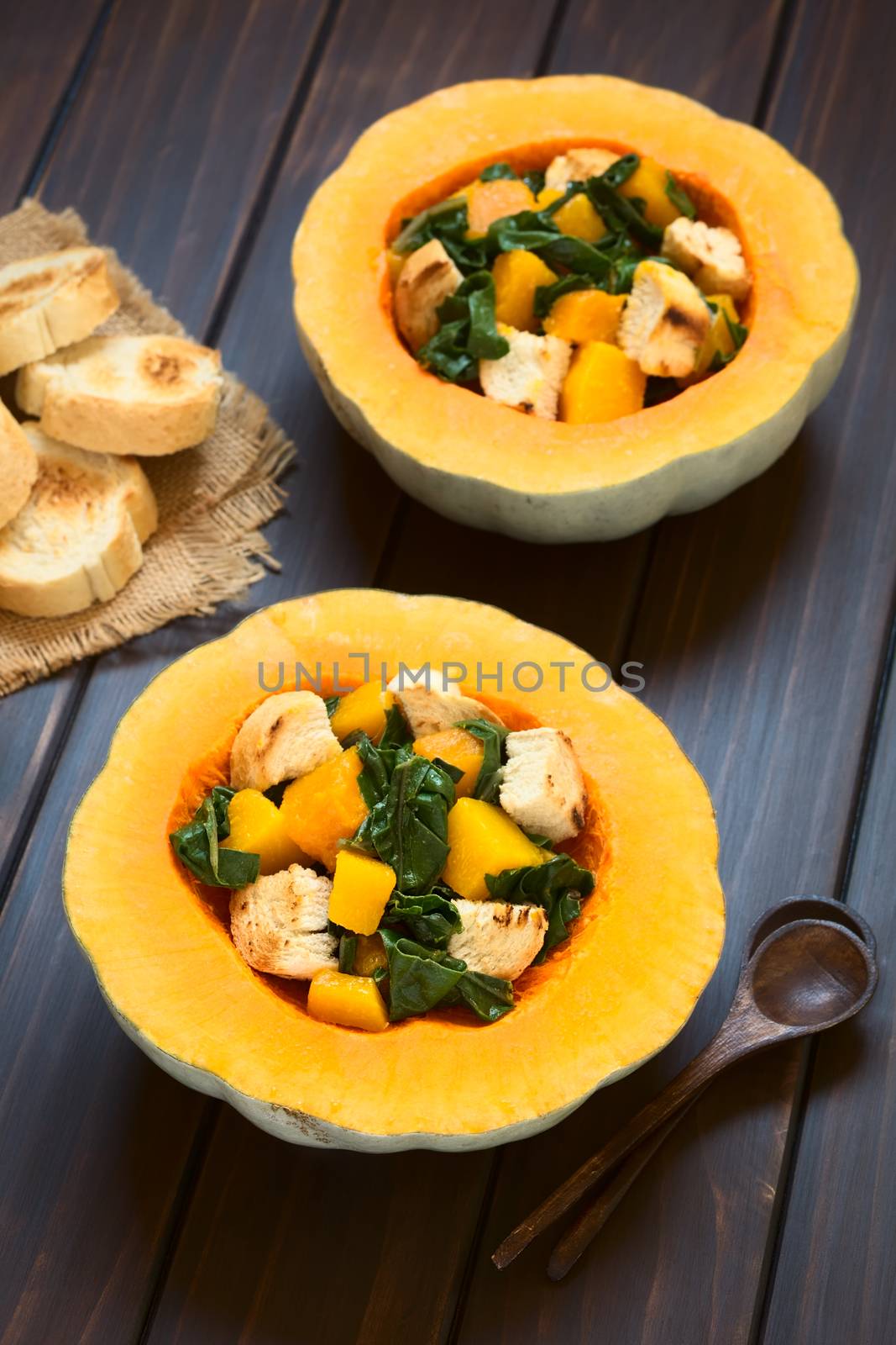 Pumpkin and chard salad with croutons served in pumpkin halves, photographed on dark wood with natural light (Selective Focus, Focus on the lower half of the first salad) 