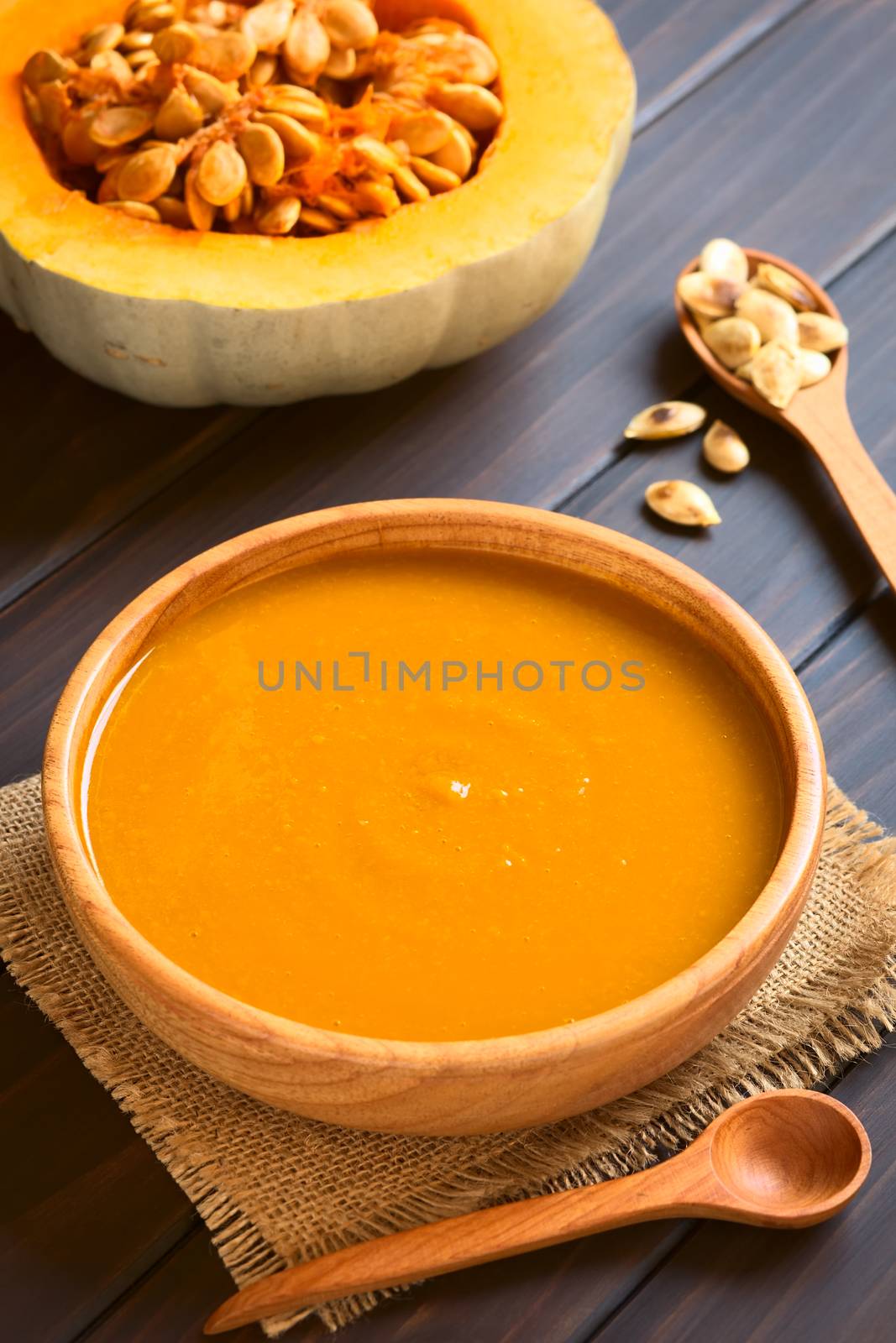 Cream of pumpkin soup served in wooden bowl, photographed on dark wood with natural light (Selective Focus, Focus on the middle of the soup) 