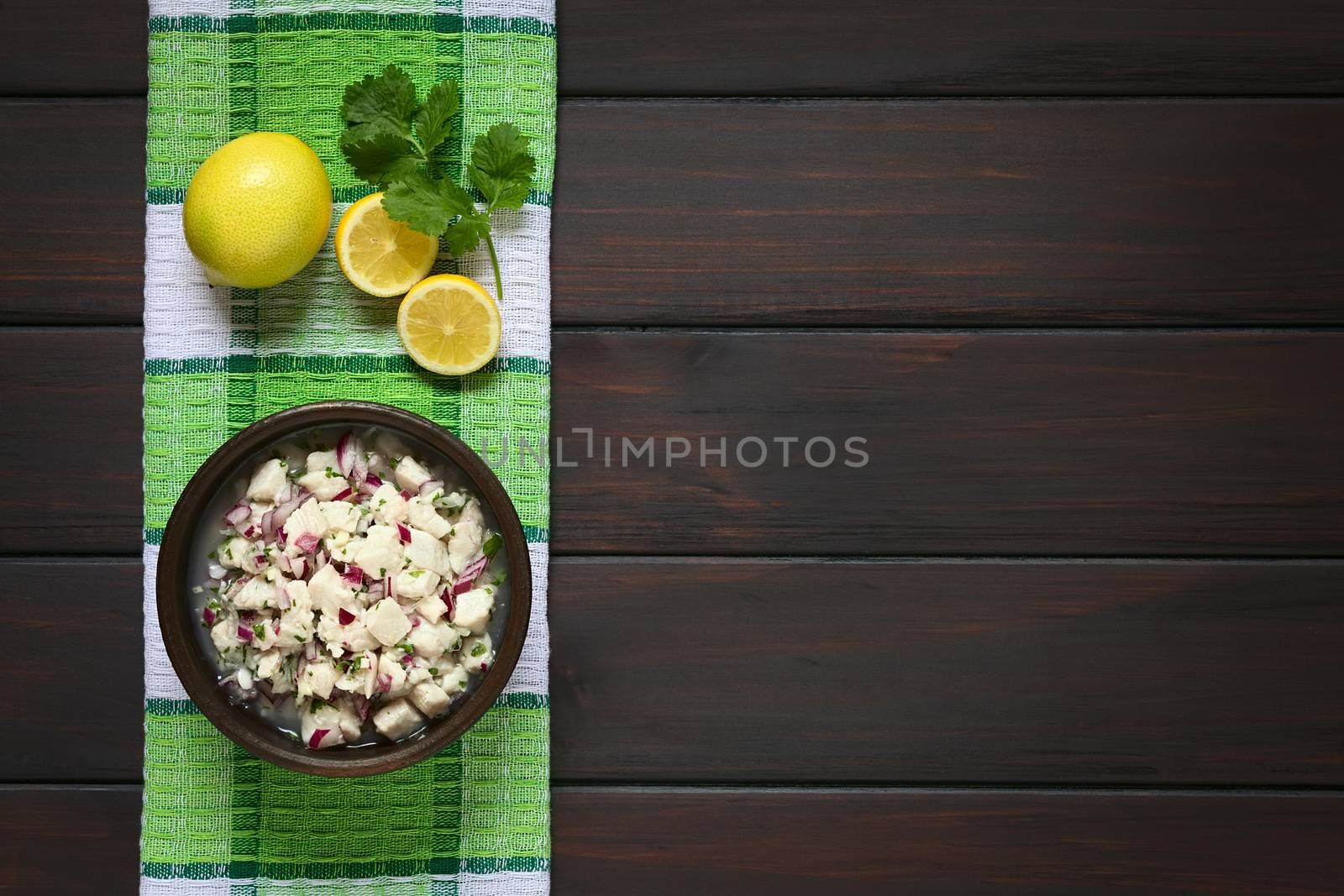 Chilean Ceviche made of Southern Ray's bream fish (lat. Brama Australis, Spanish Reineta), onion, garlic and cilantro marinated in lemon juice. Photographed overhead on dark wood with natural light.