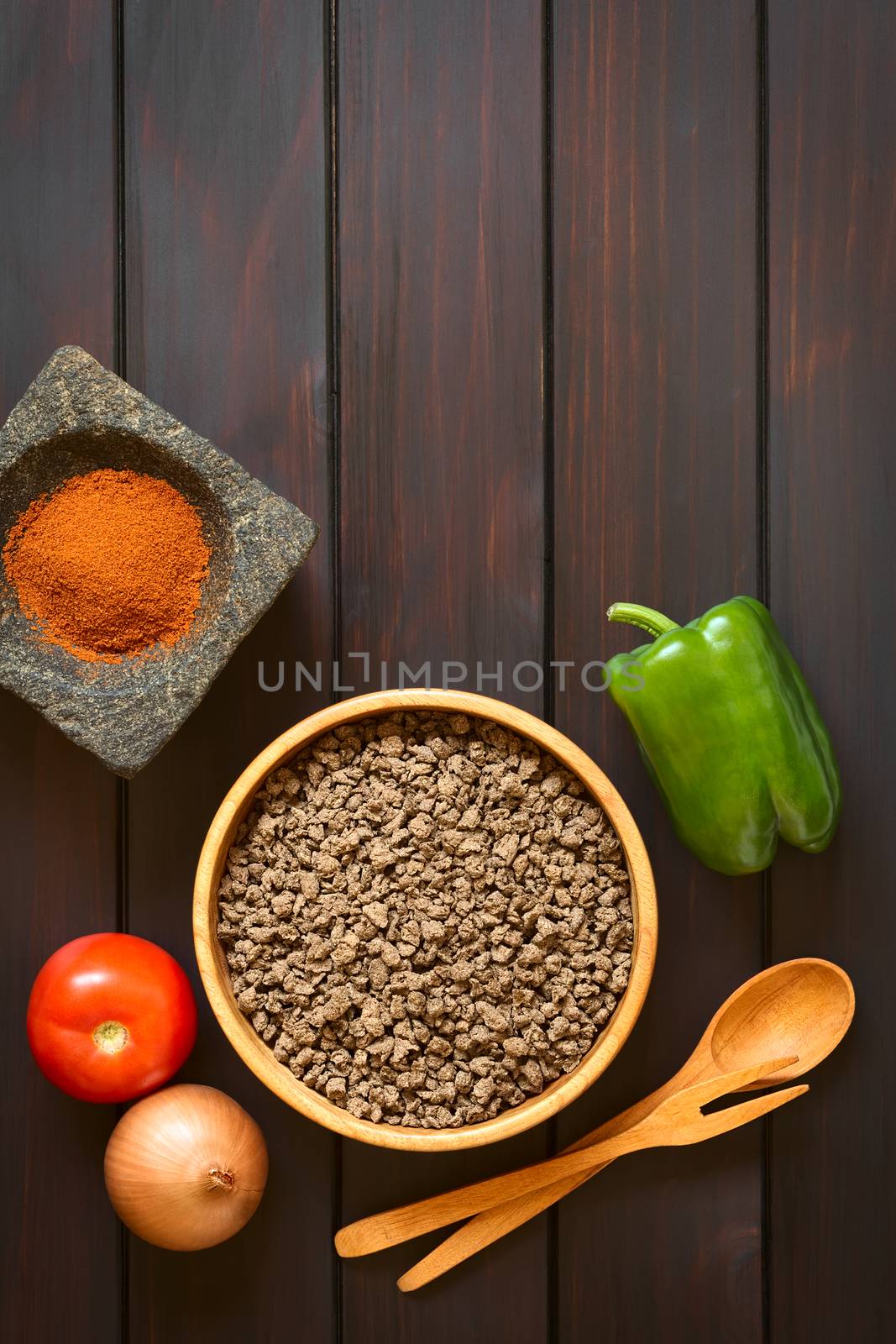 Raw textured vegetable or soy protein, called also soy meat in wooden bowl with raw vegetables and paprika in mortar. Photographed overhead on dark wood with natural light. 