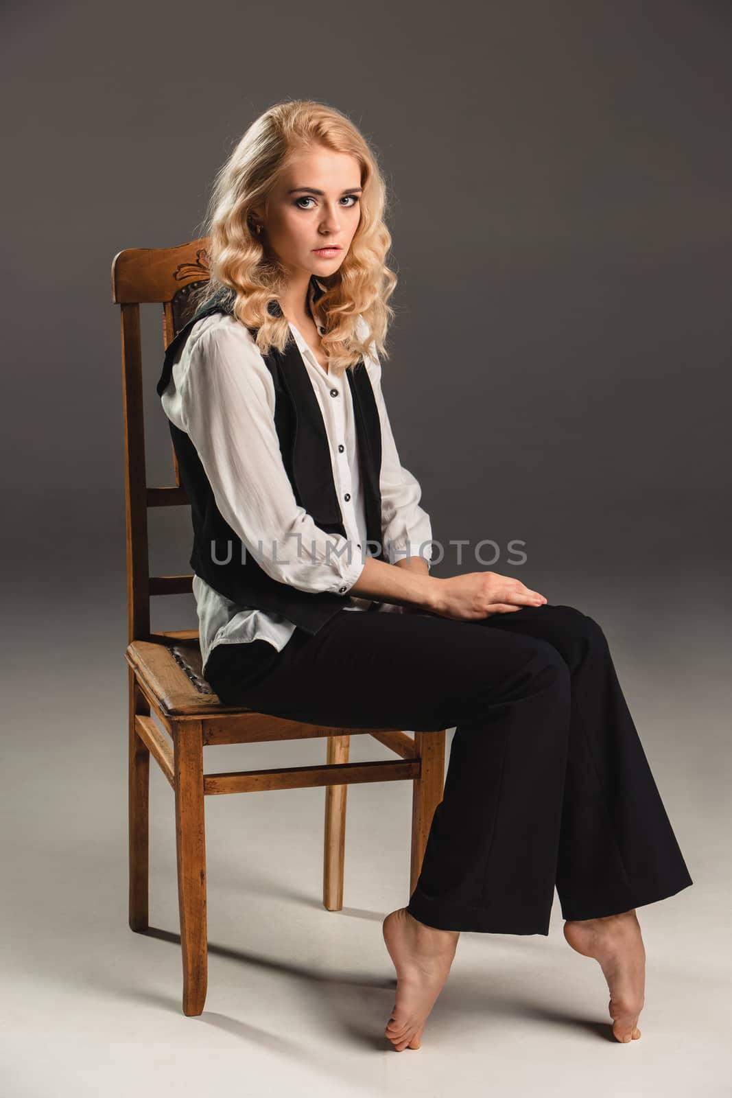Beauty blond woman  in a black suit on chair on a gray background