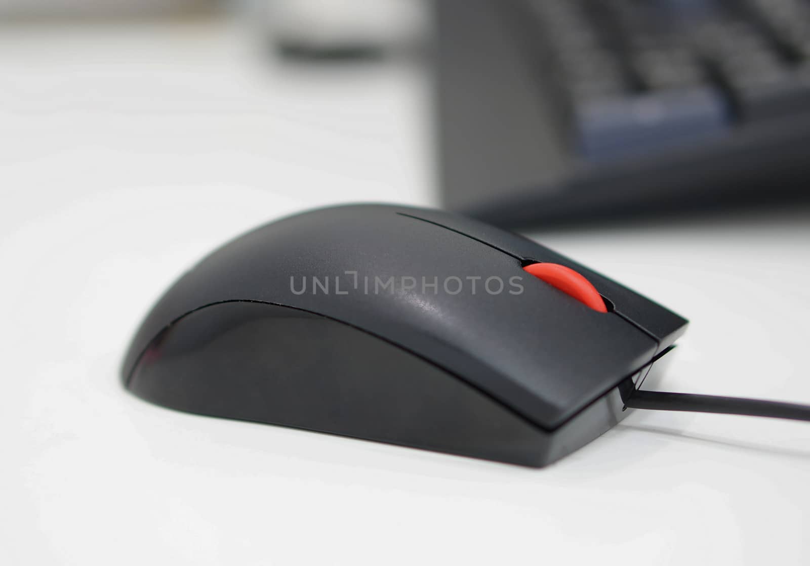Computer mouse has a black wire attached to the PC, scrolling button is red in the middle.                               