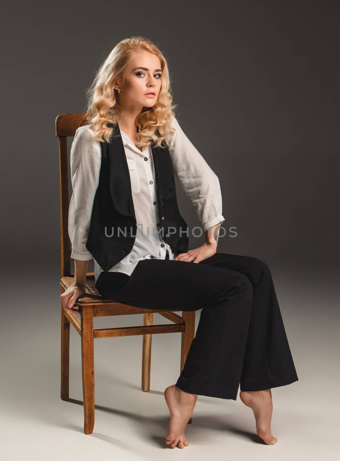 Beauty blond woman  in a black suit and white shirt, sitting on a chair on a gray background