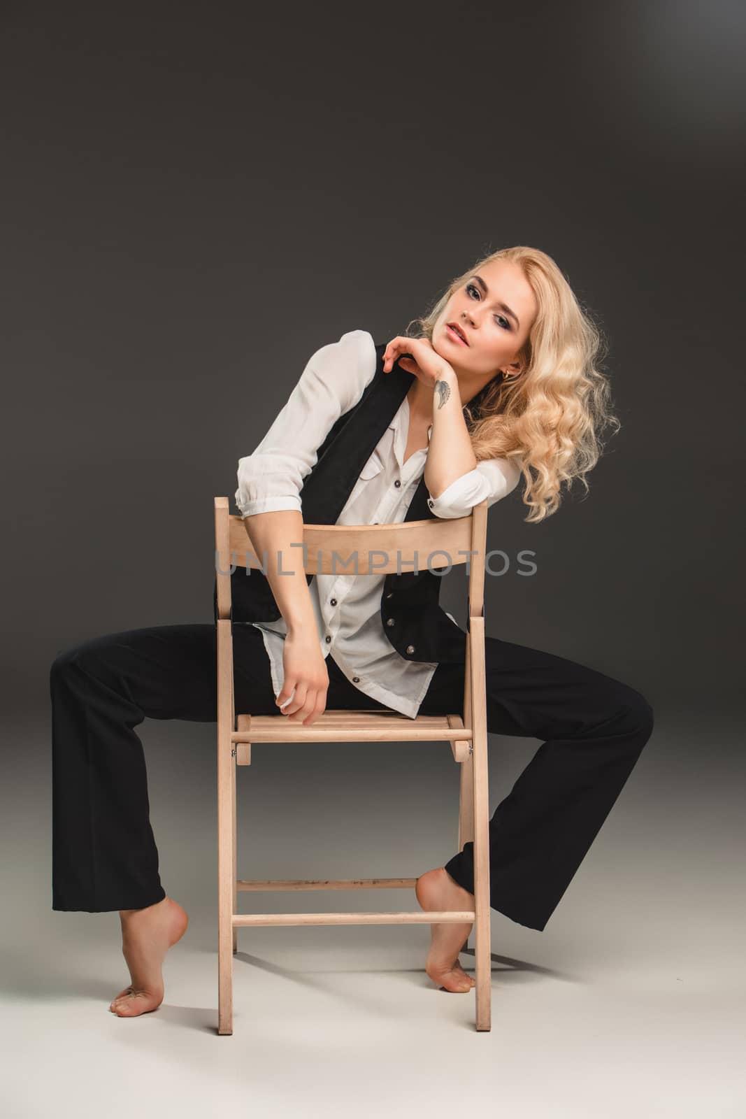 Beauty blond woman  in a black suit and white shirt, sitting on a chair on a gray background