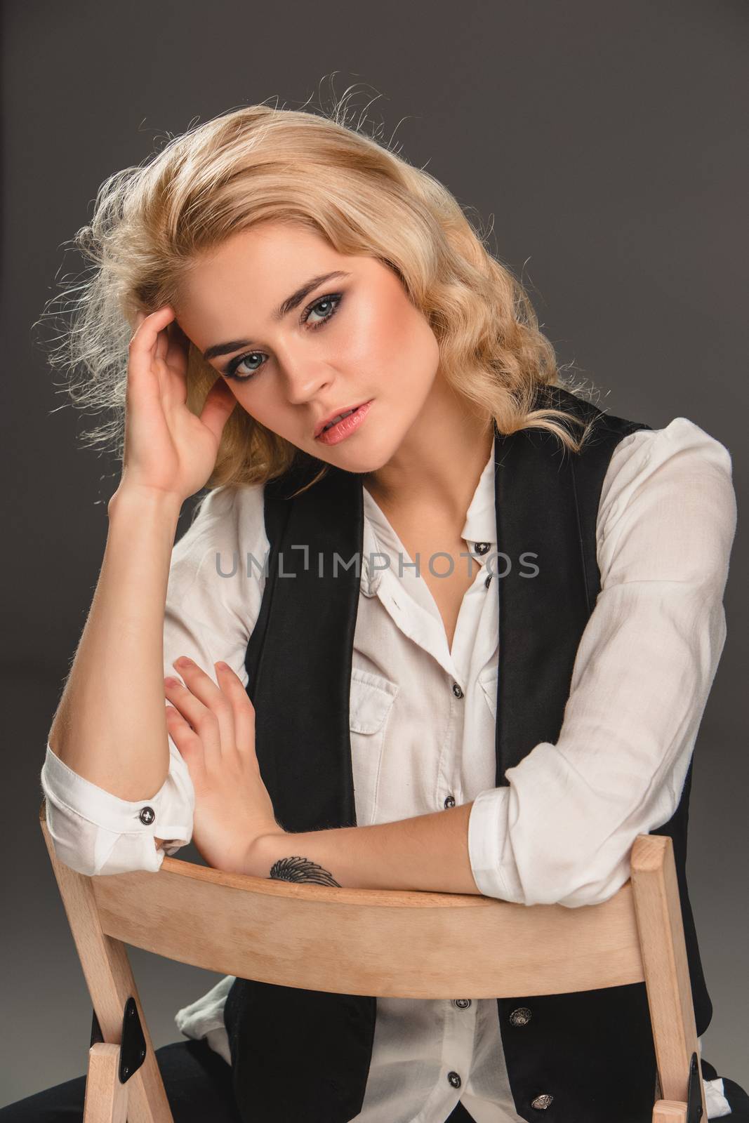 Beauty blond woman  in a black suit and white shirt, sitting on a chair on a gray background