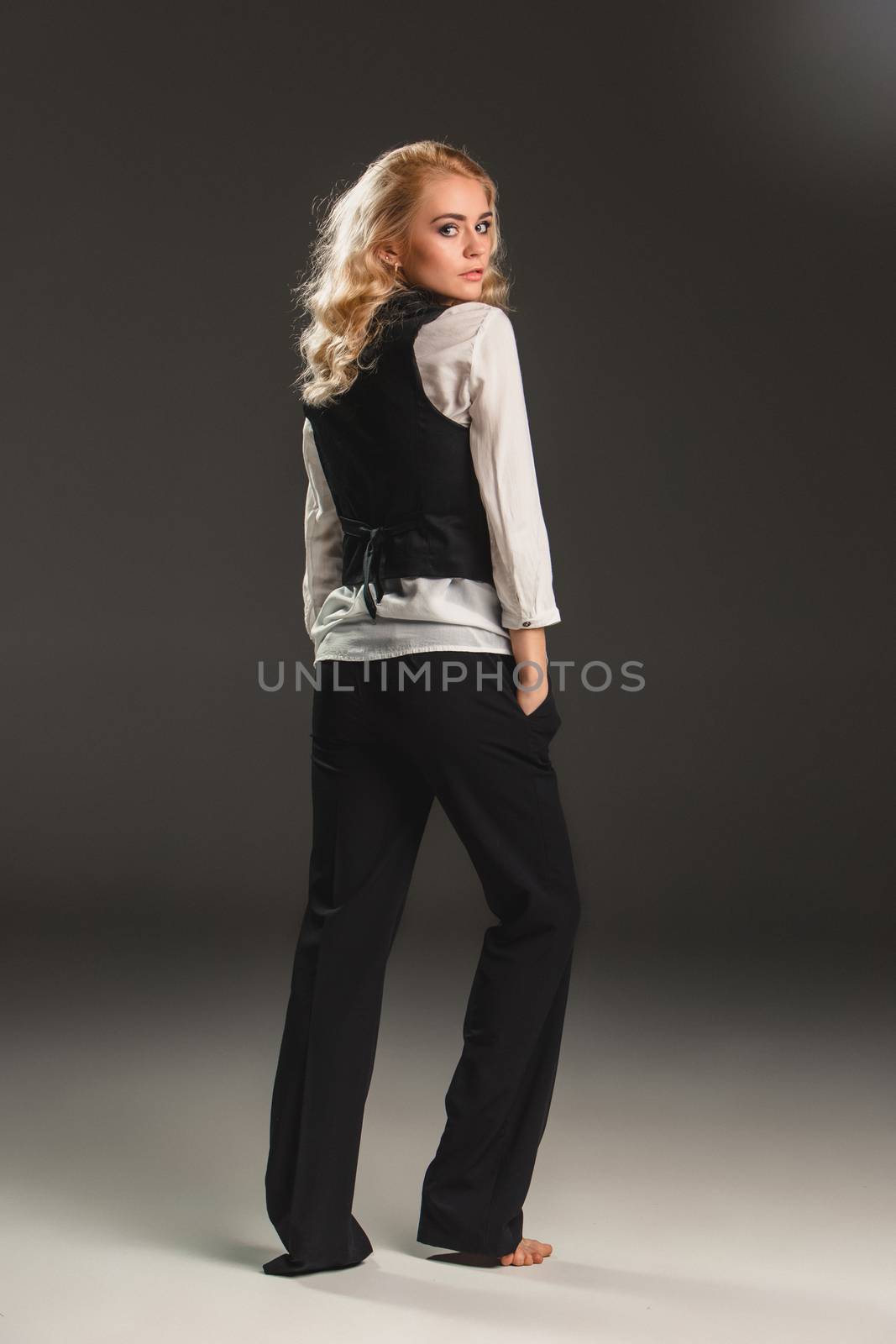 Beauty blond woman  in a black suit and white shirt on a gray background. Portrait in full growth