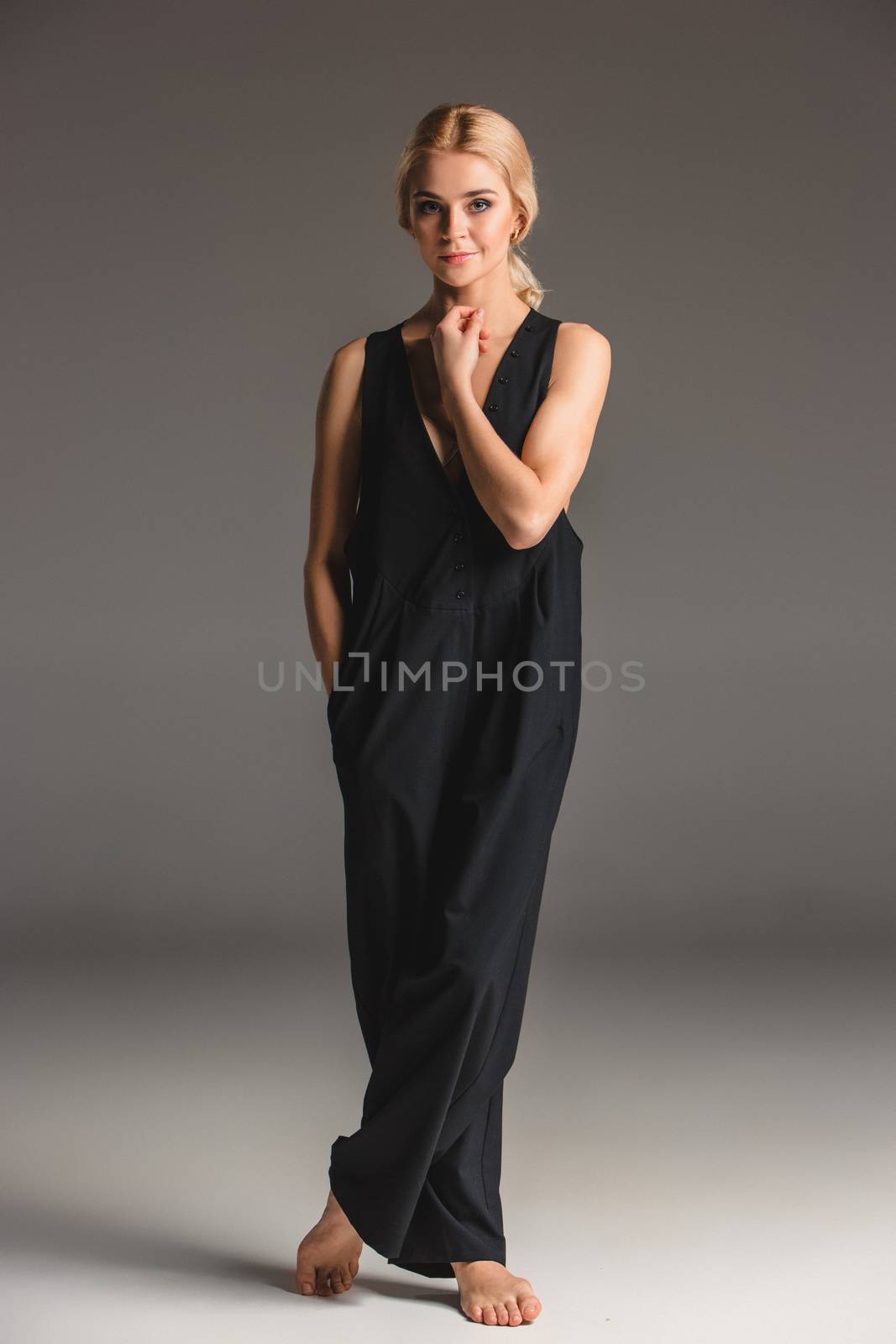 Beauty blond woman  in a black coveralls on a gray background. Portrait in full growth