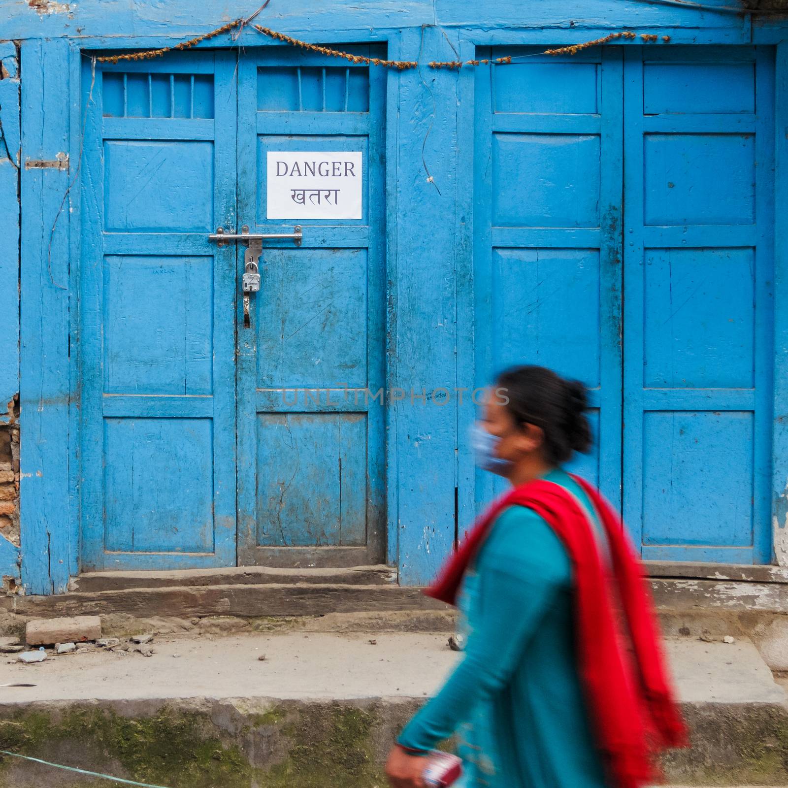 KATHMANDU, NEPAL - MAY 11, 2015: A woman walks past a danger sign on an old traditional house in Handigaun.