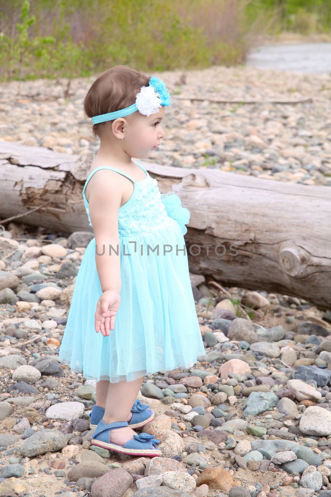 Little girl wearing a blue dress on pebble beach