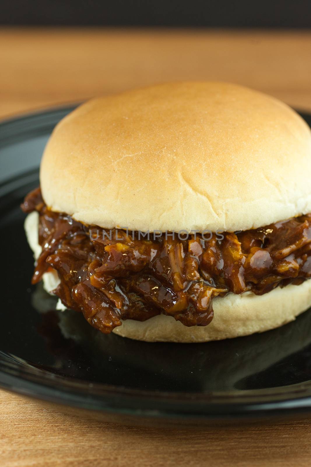 A barbecue pork sandwich on a black plate on a wooden counter top.