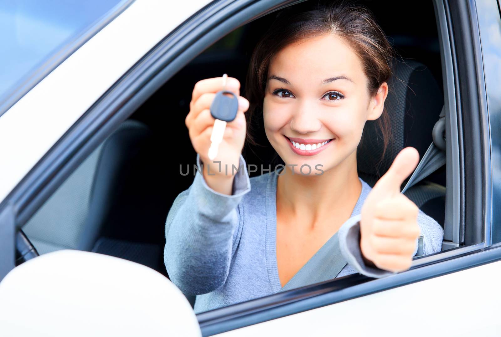 Happy girl in a car showing a key and thumb up gesture