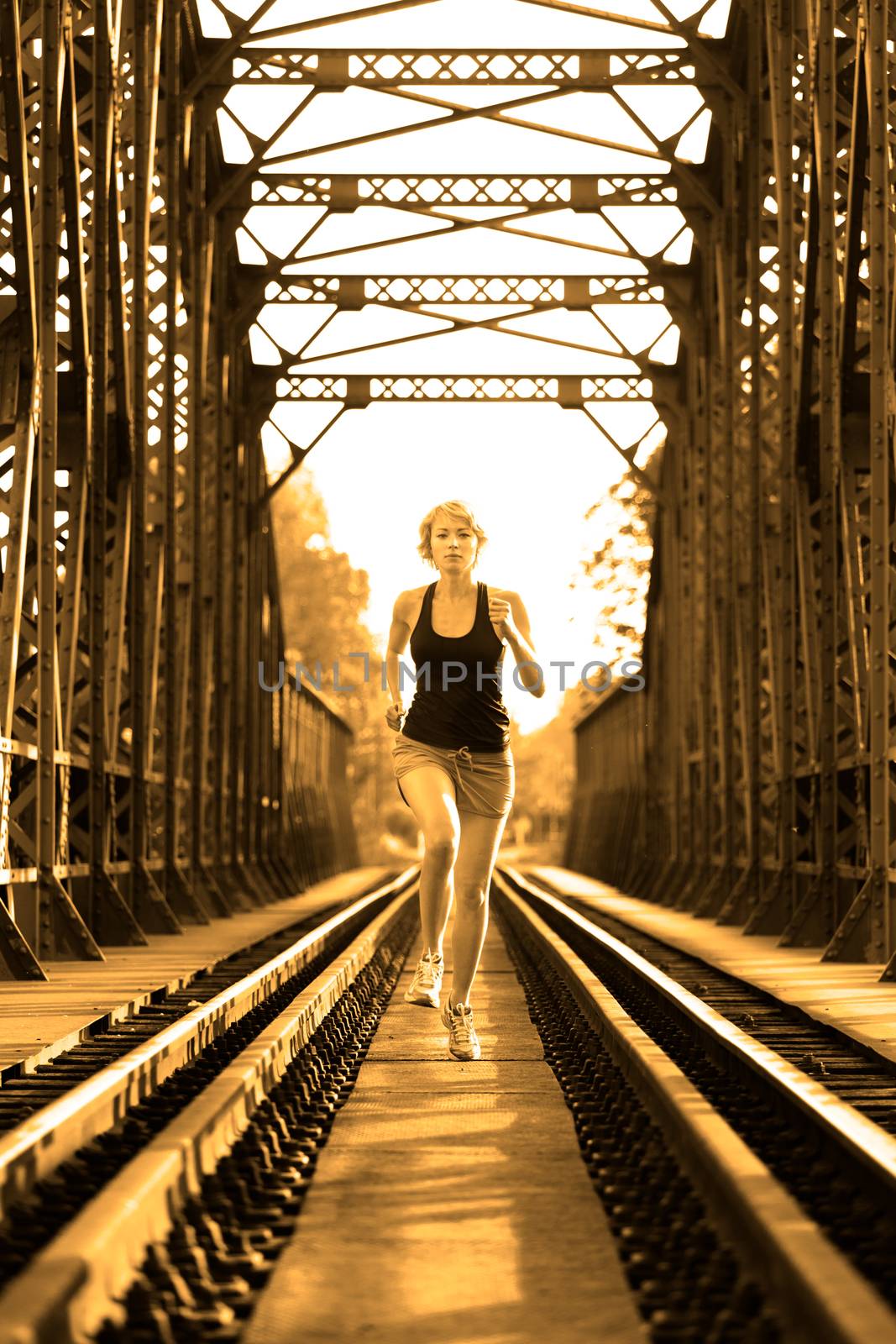 Athlete running on railaway tracks bridge in morning sunrise training for marathon and fitness. Healthy sporty caucasian woman exercising in urban environment. Active urban lifestyle.