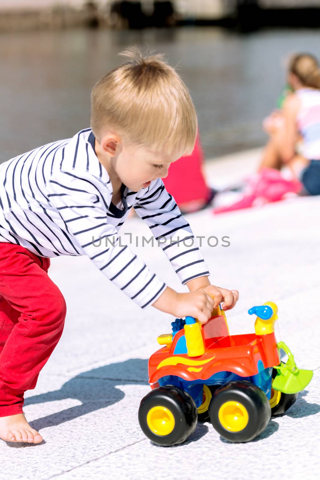 Little preschool boy playing with big toy car and having fun, outdoors.