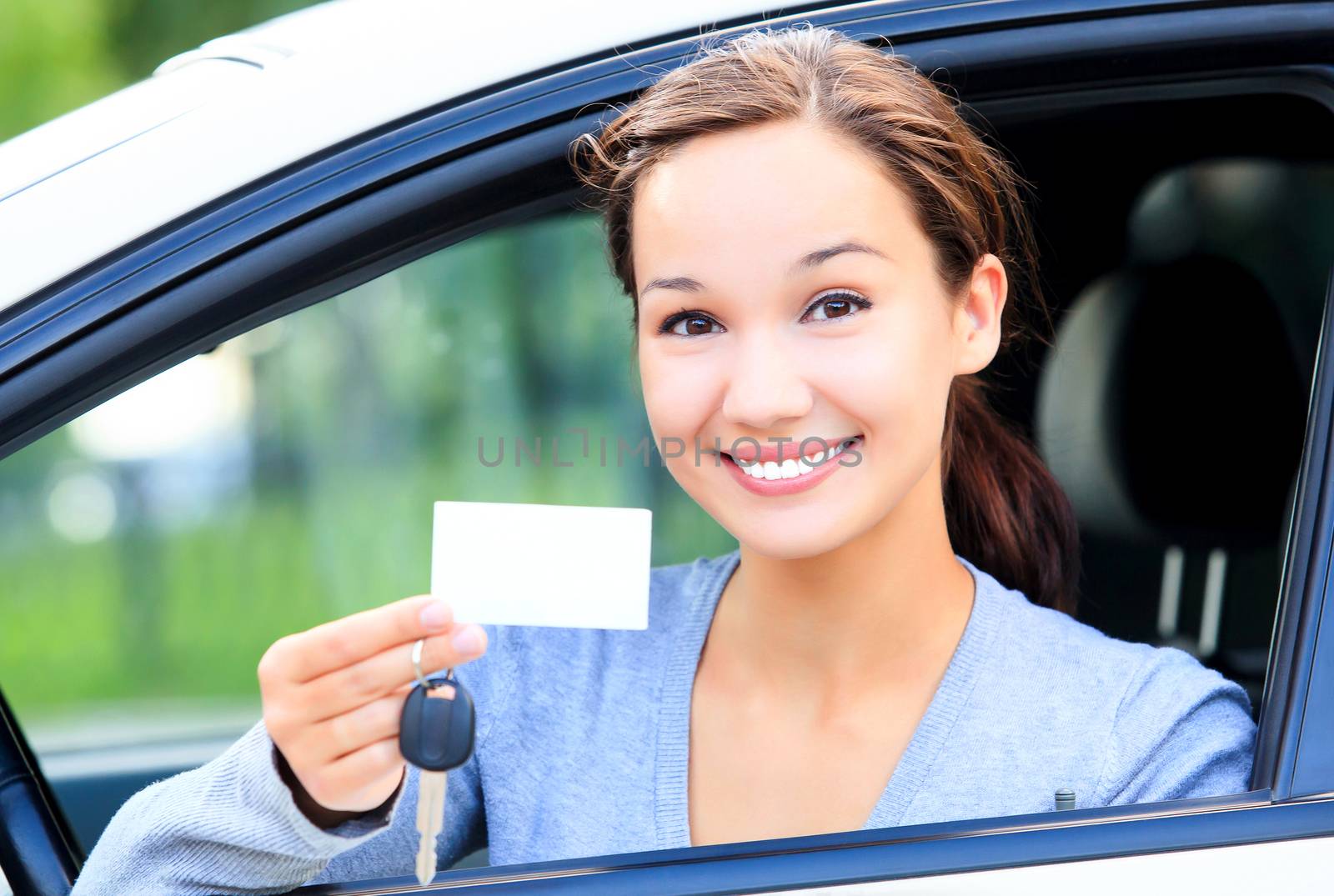 Happy girl in a car showing a key and an empty white card for your message