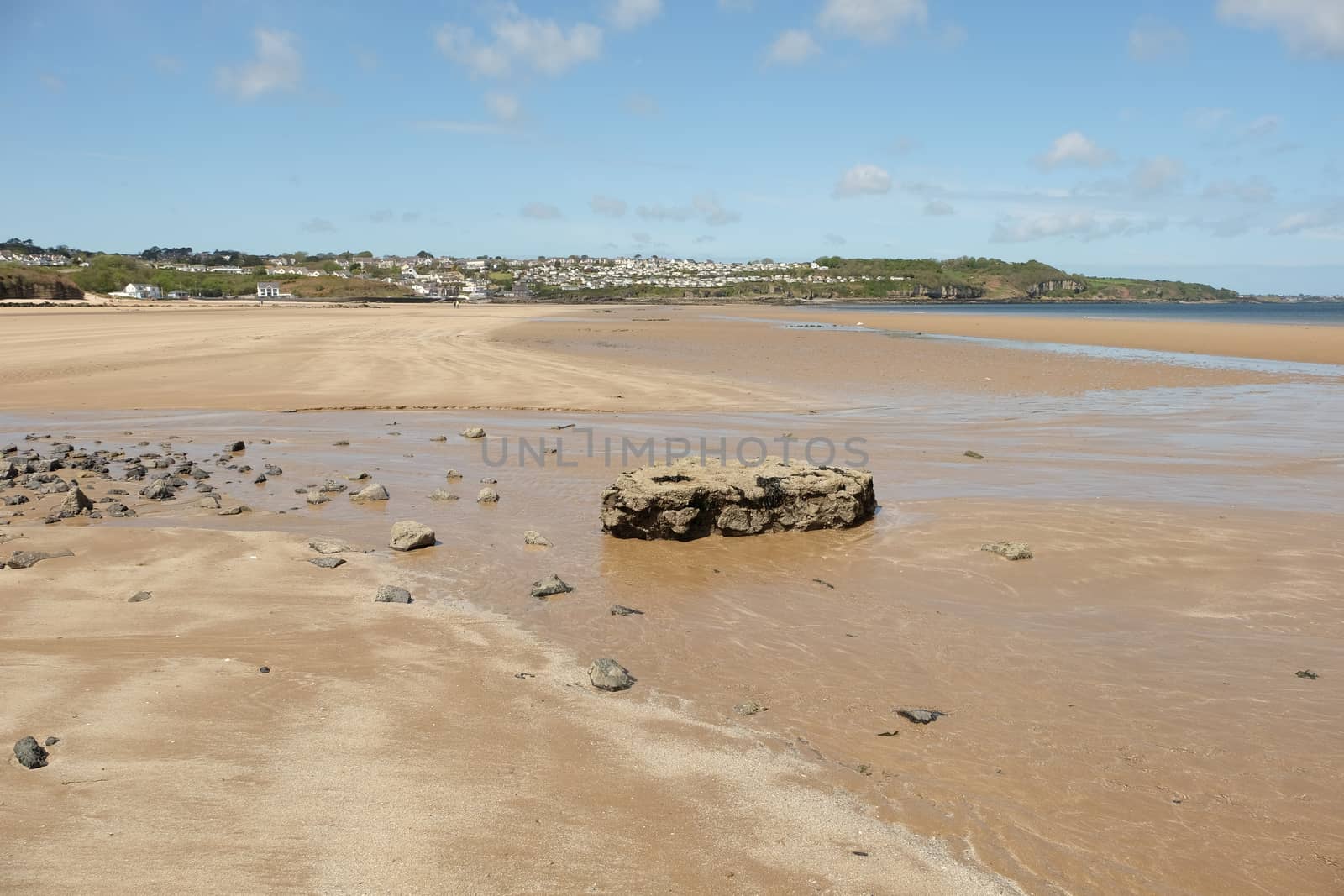 A view from a stream and rocks across the deserted clean sandy beach to the holiday village of Benllech, Anglesey, Wales, UK.