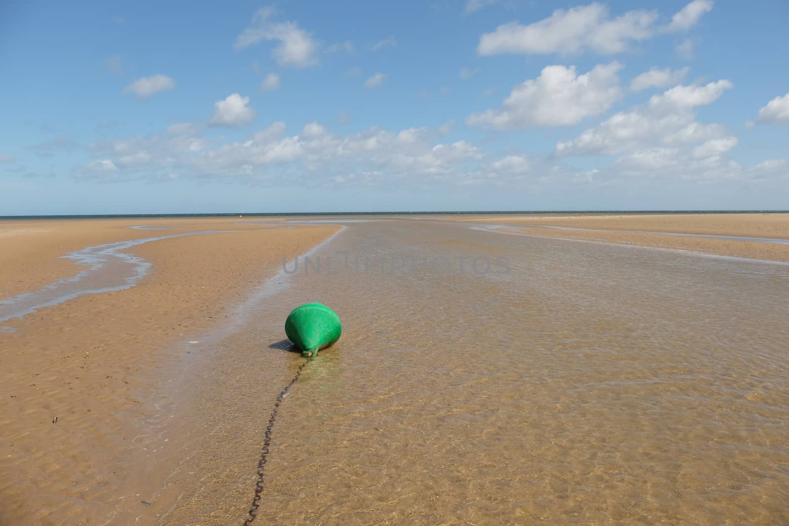 A chained channel day marker, green, can buoy, at low water looking out to sea,