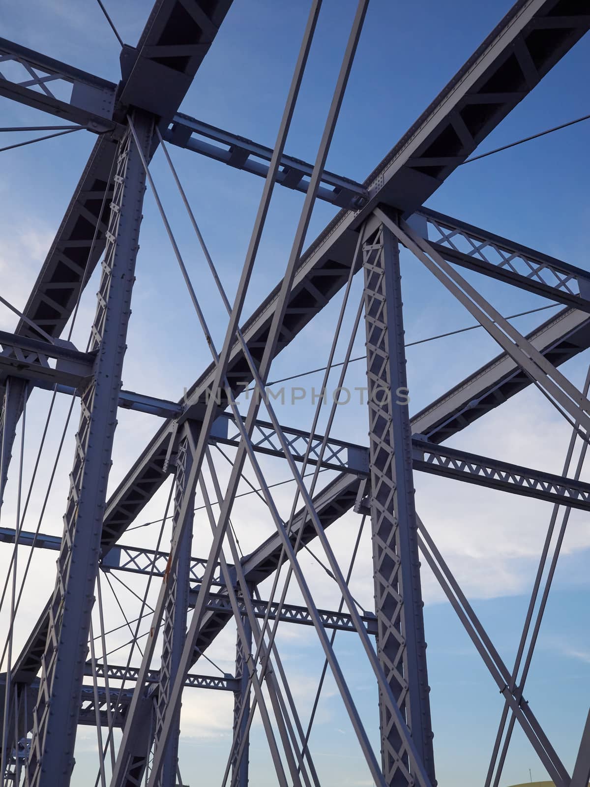 Detail shot of an historic gray painted Dutch riveted truss bridge against a blue sky.