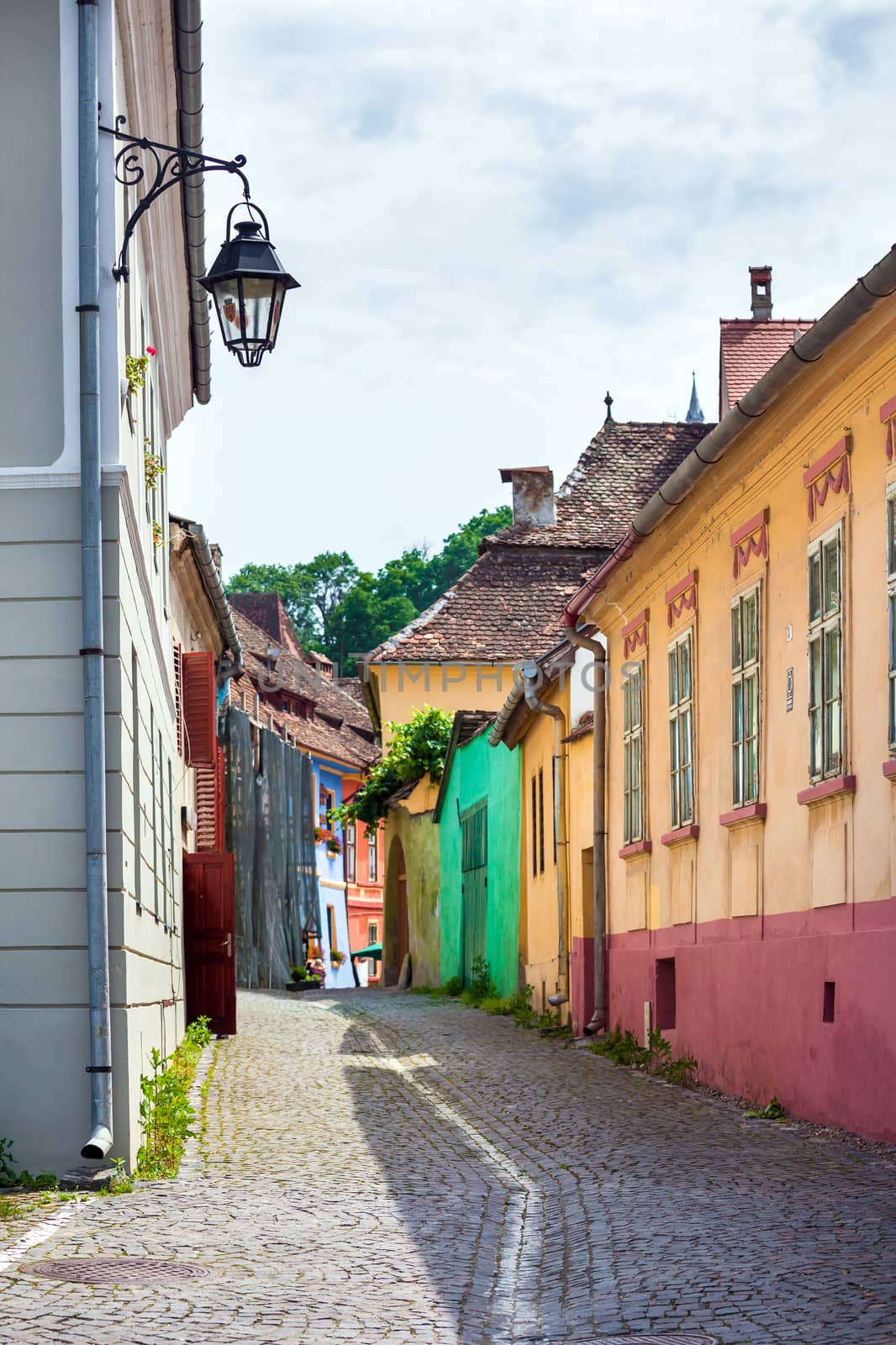 Sighisoara, Romania - June 23, 2013: Street lamp on old stone paved street with colored house from Sighisoara fortresss, Transylvania, Romania