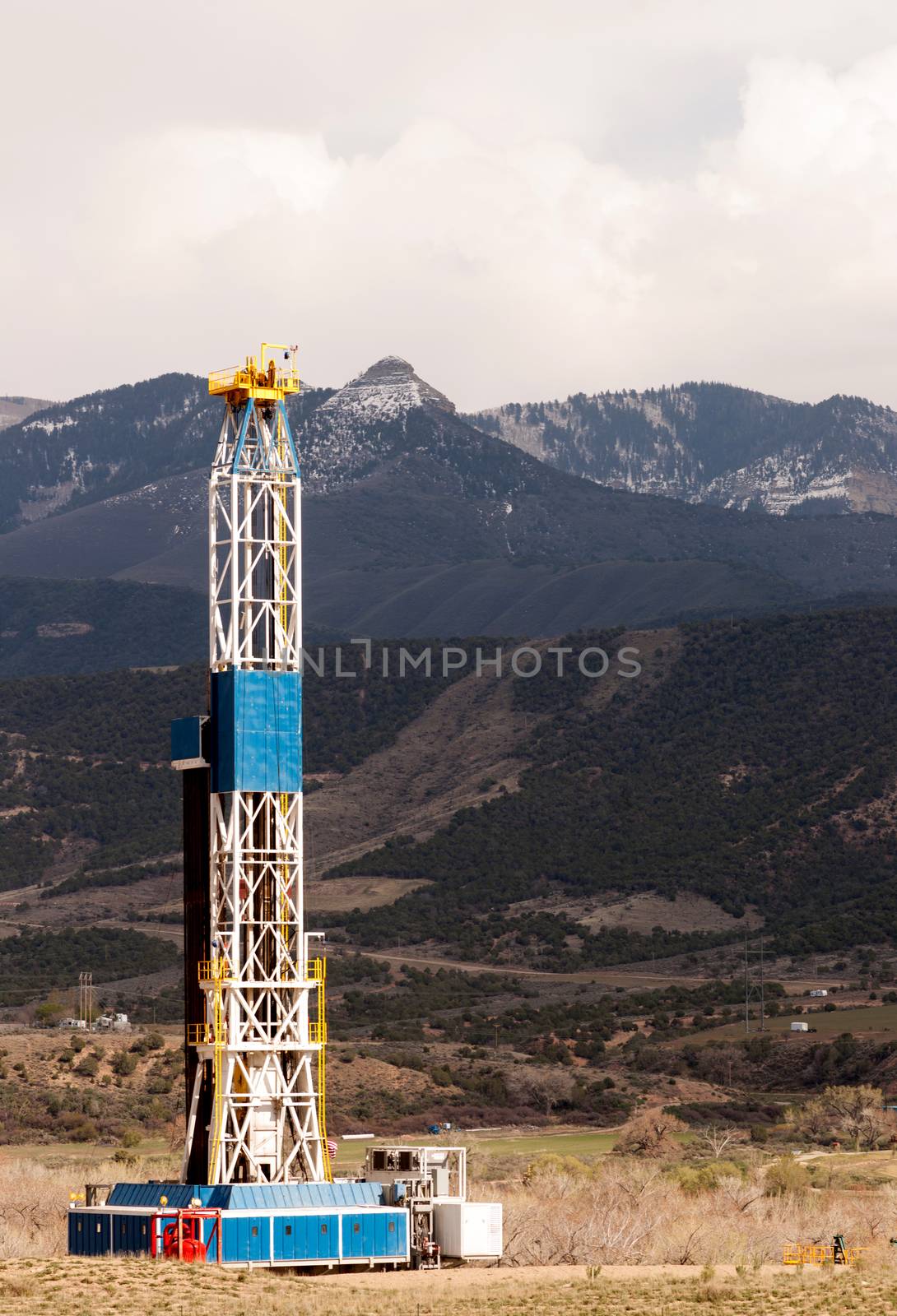 An oil derrick stands late in the day against the mountains