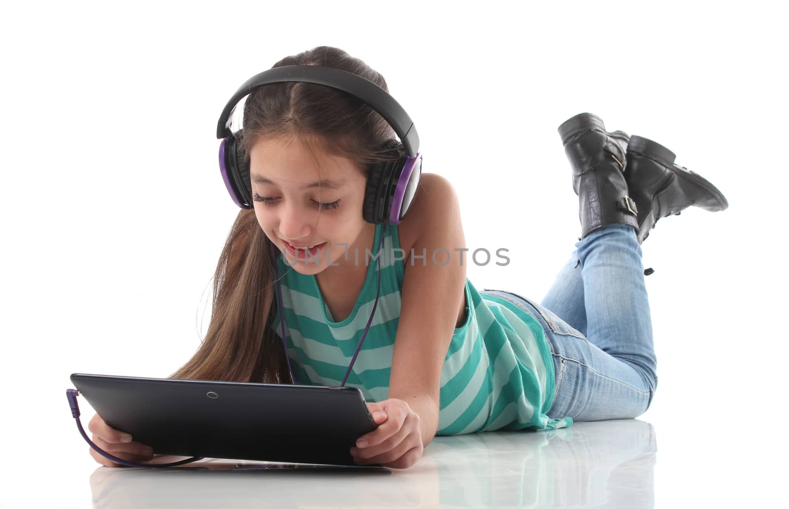 Beautiful pre-teen girl on the floor, usin a tablet computer and headphones, white background