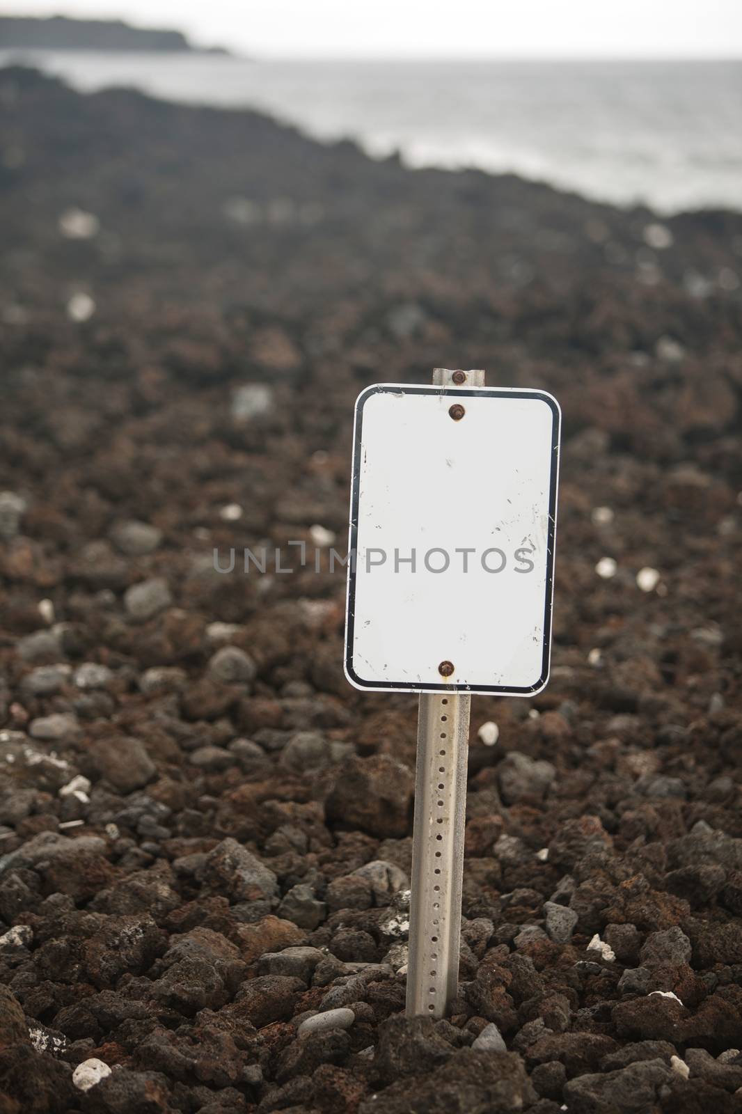 Blank white sign on beach of volcanic rock