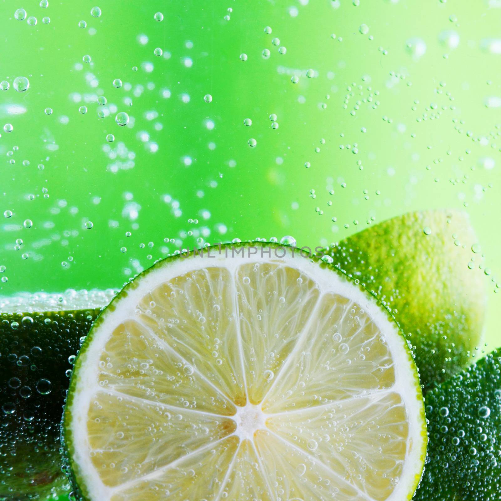 Cut limes in the water with bubbles on green background