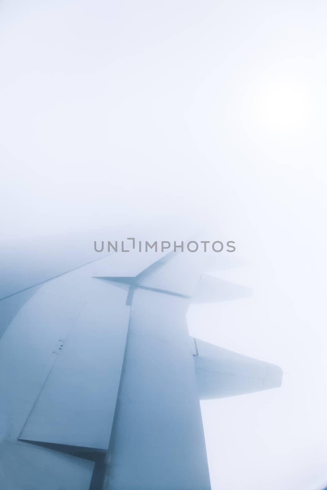 Window view of wing of an jet airplane with deep blue sky and the sun in the background