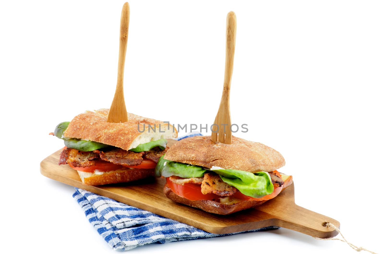 Ciabatta Sandwiches with Bacon, Tomato, Lettuce and Sauces on Cutting Board Arranged with Wooden Fork isolated on white background