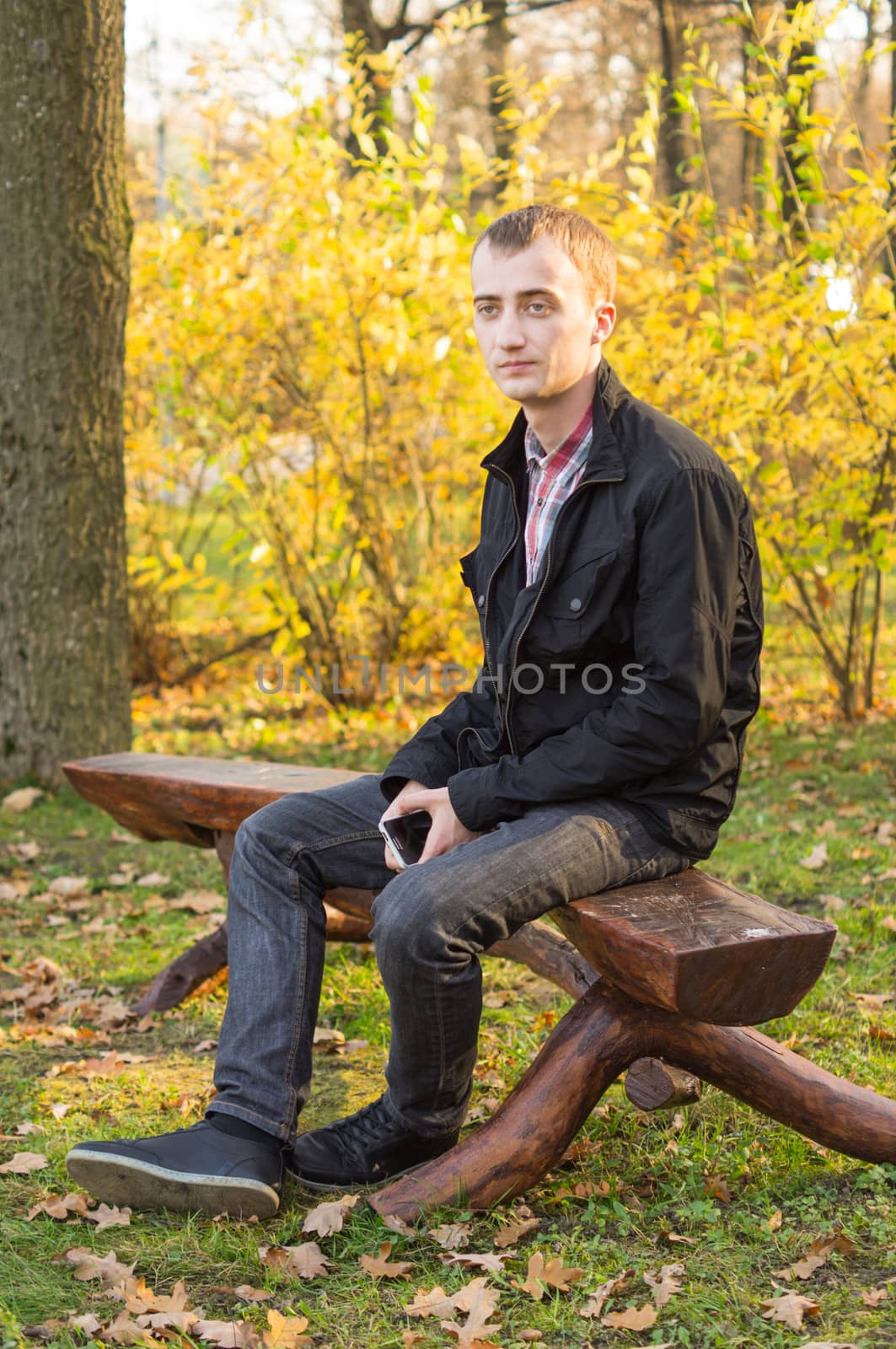 young attractive man a black jacket in autumn park by serhii_lohvyniuk