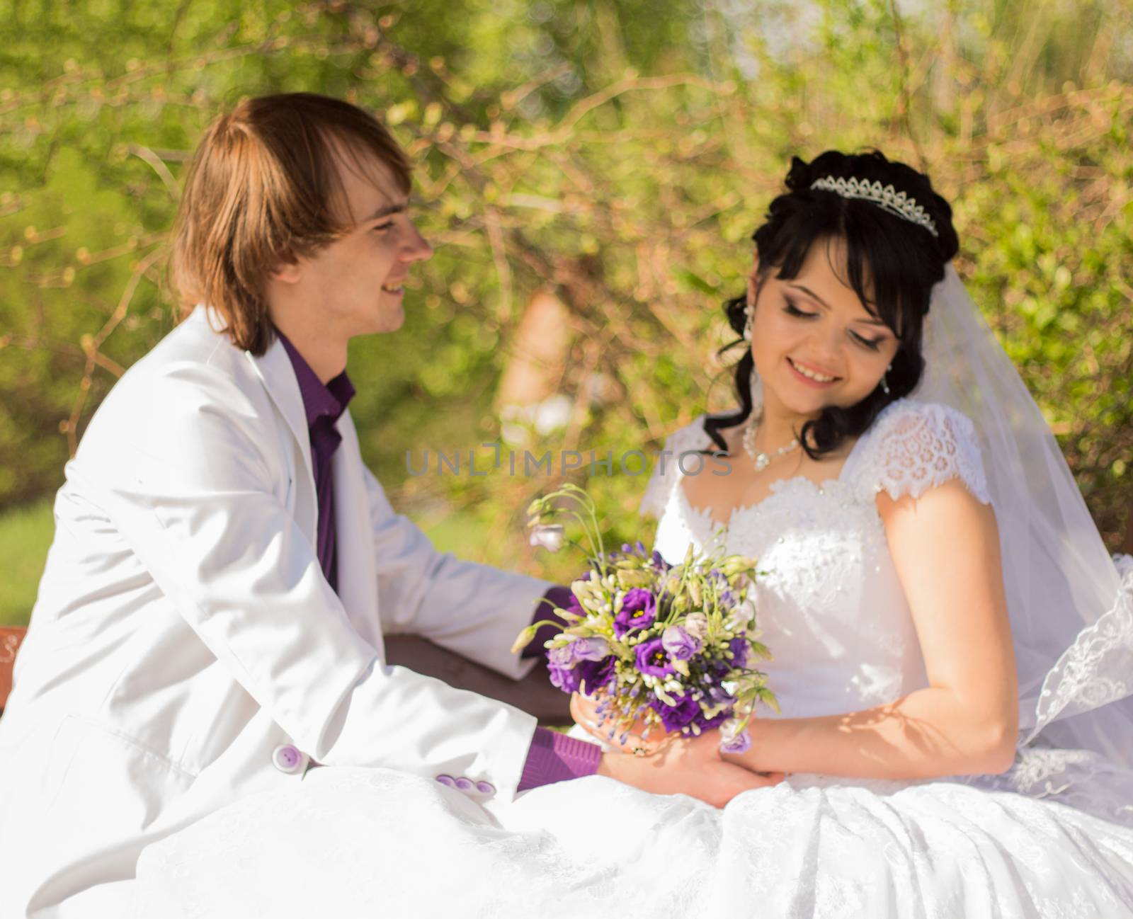 Romantic wedding couple sitting on a bench in the park.