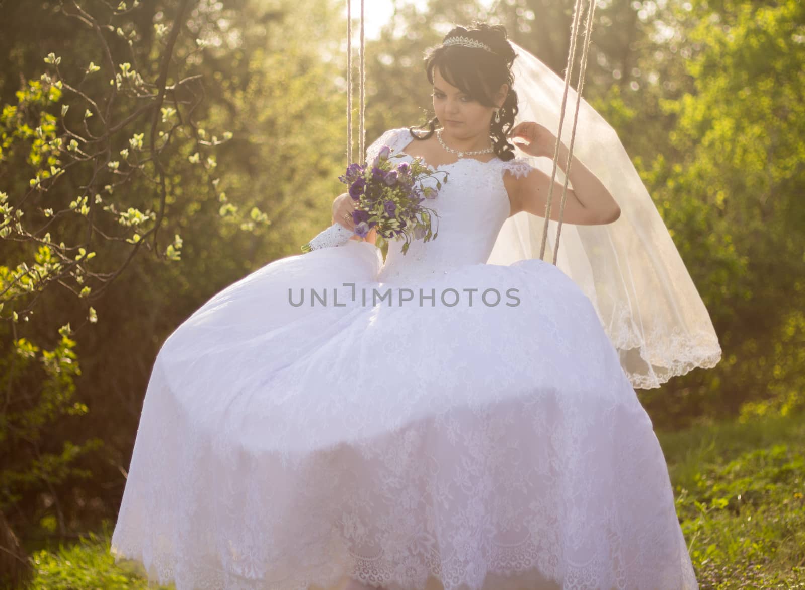 Portrait of a beautiful bride in white wedding dress sitting on swing outdoors