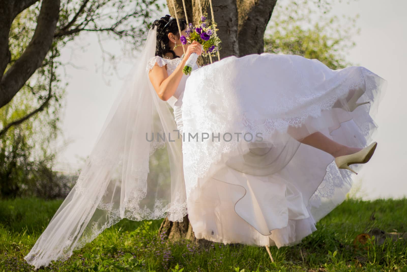 Portrait of a beautiful bride in white wedding dress sitting on swing outdoors