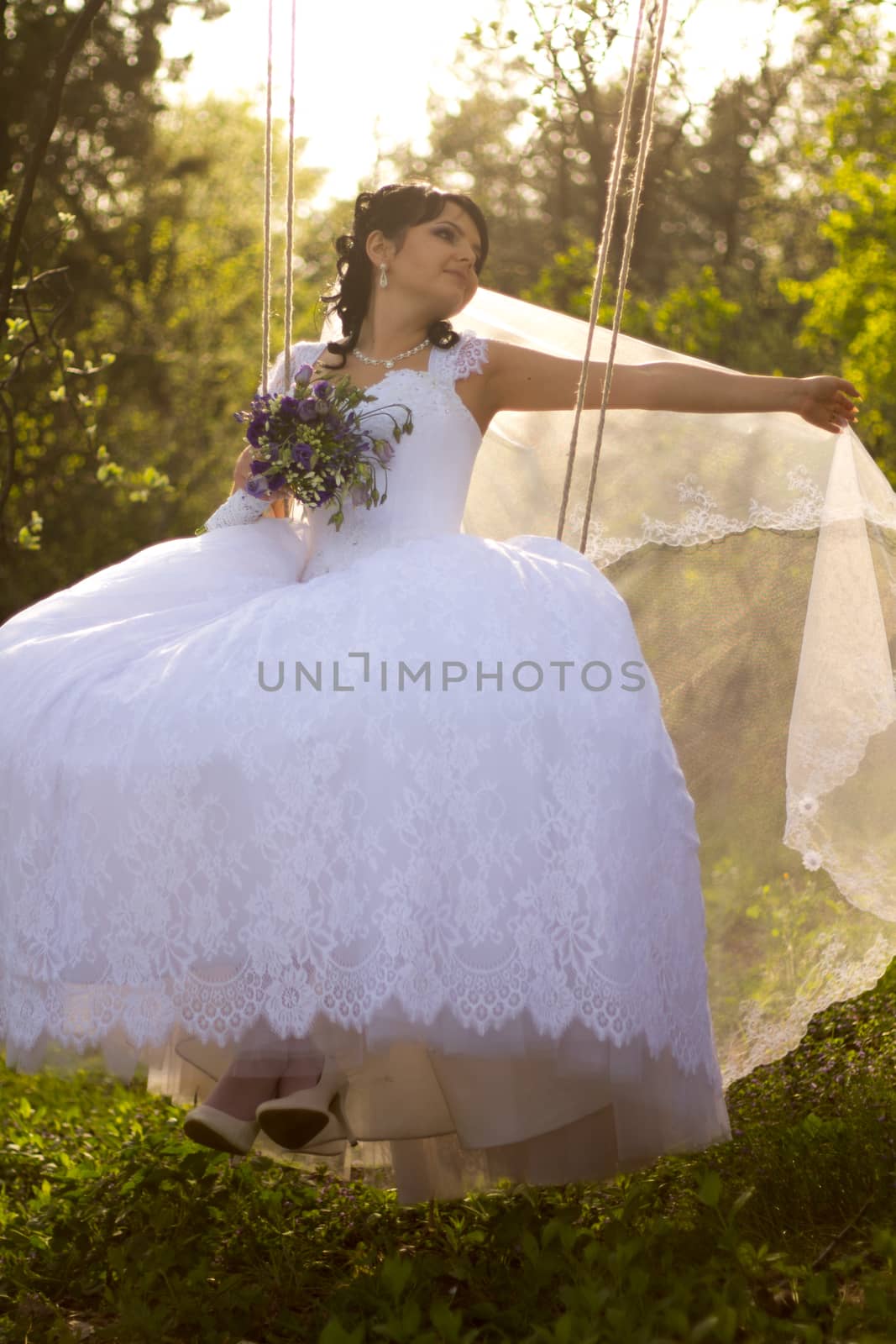 Portrait of a beautiful bride in white wedding dress sitting on swing outdoors