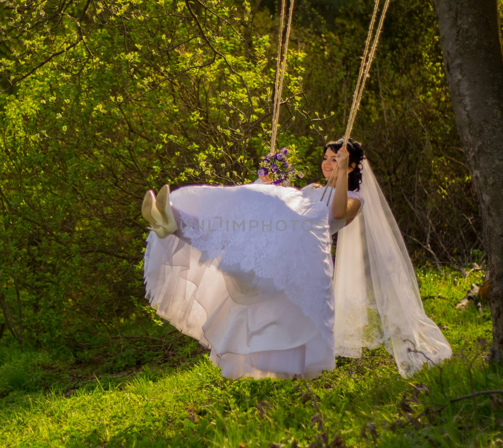 Portrait of a beautiful bride in white wedding dress sitting on swing outdoors