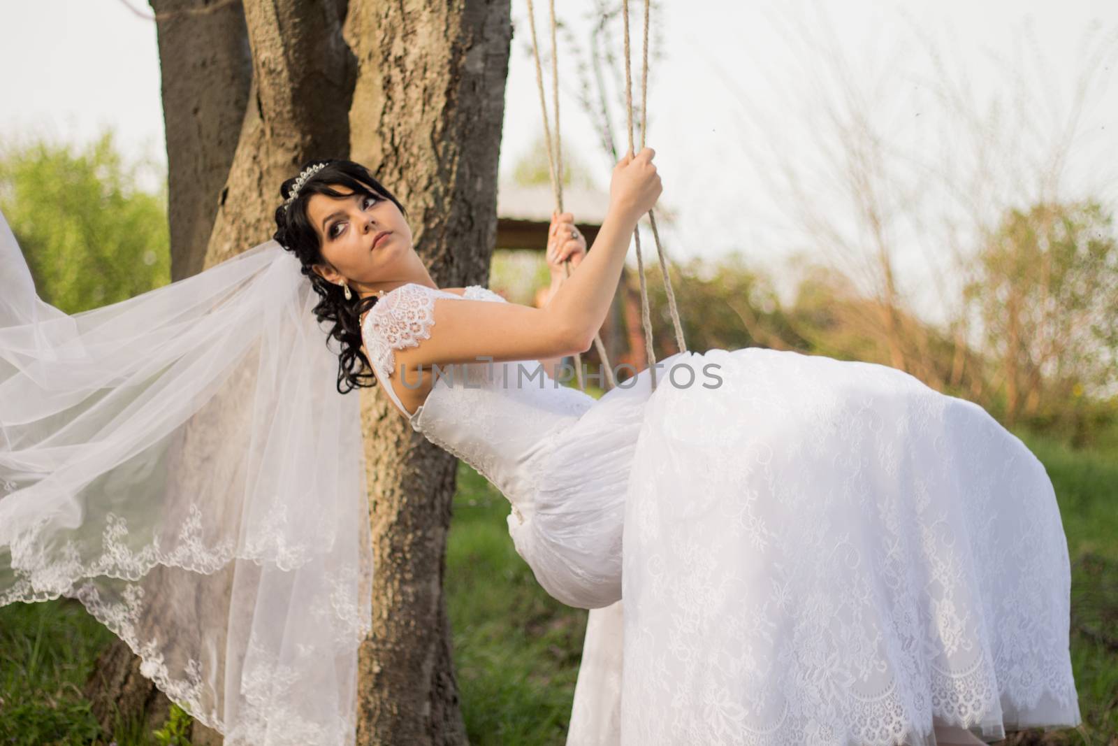 Portrait of a beautiful bride in white wedding dress sitting on swing outdoors