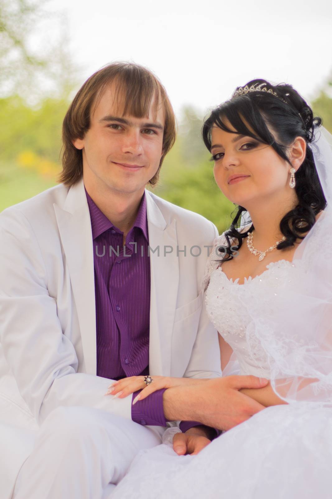 Couple in love bride and groom posing sitting on wooden bench in gazebo in their wedding day in summer.