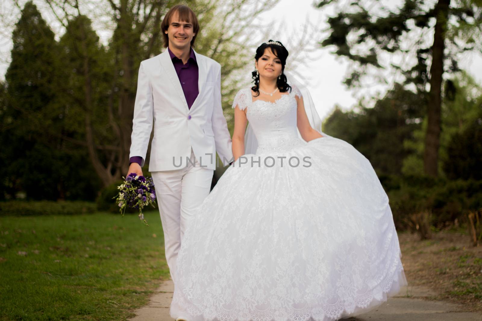 Happy bride and groom in shady alley on wedding walk by serhii_lohvyniuk