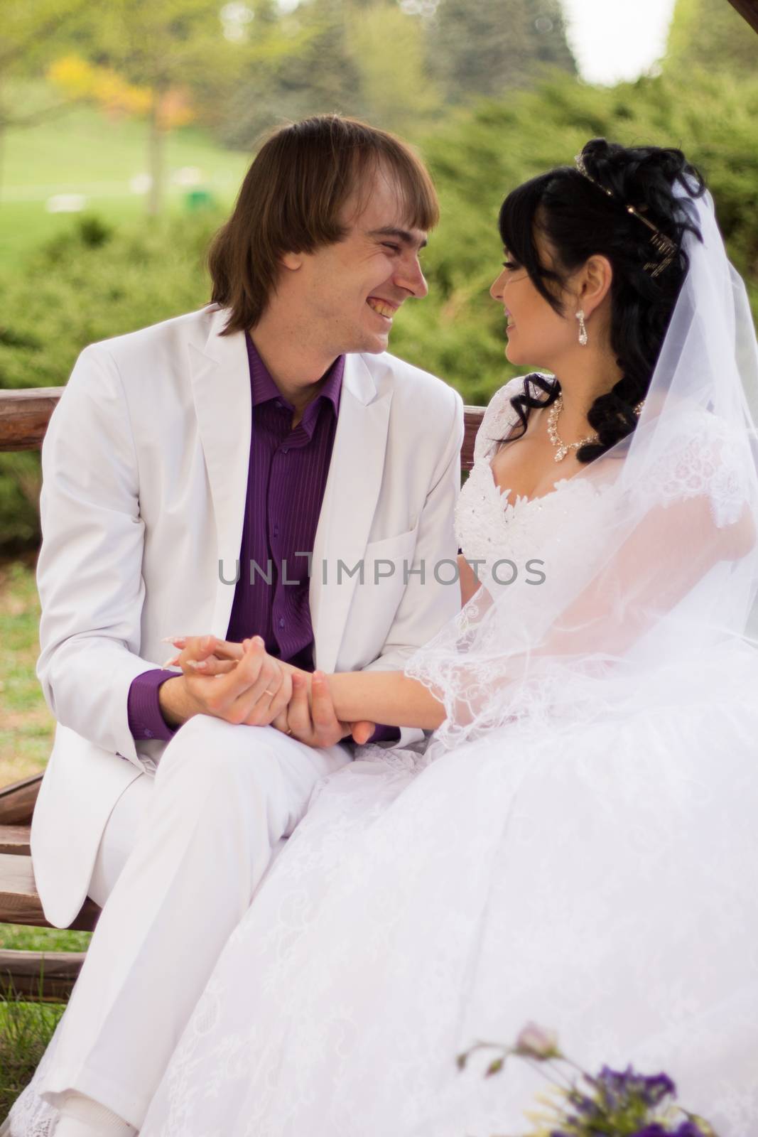 Couple in love bride and groom posing sitting on wooden bench in gazebo in their wedding day in summer.