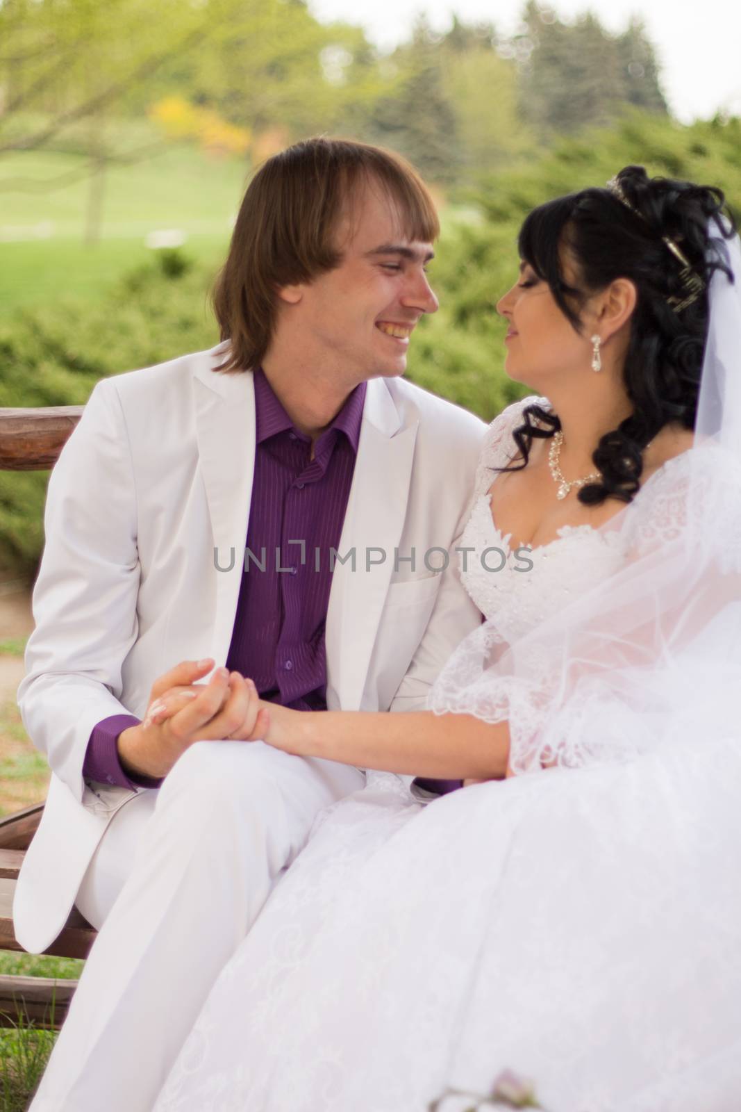 Couple in love bride and groom posing sitting on wooden bench in gazebo in their wedding day in summer.