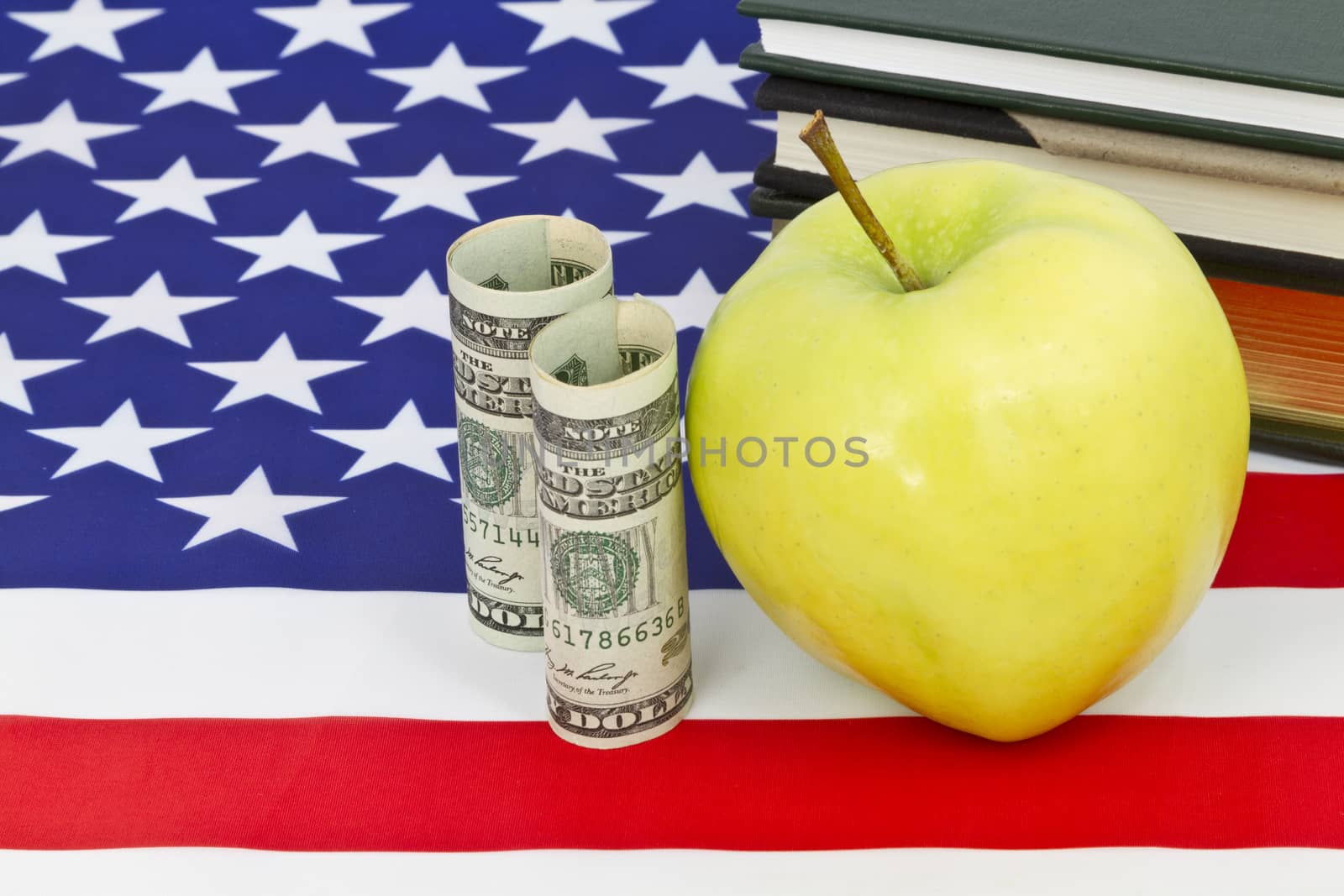 Symbolic apple representative of education placed with American currency, national flag, and books reflects emphasis on important financial support for education.