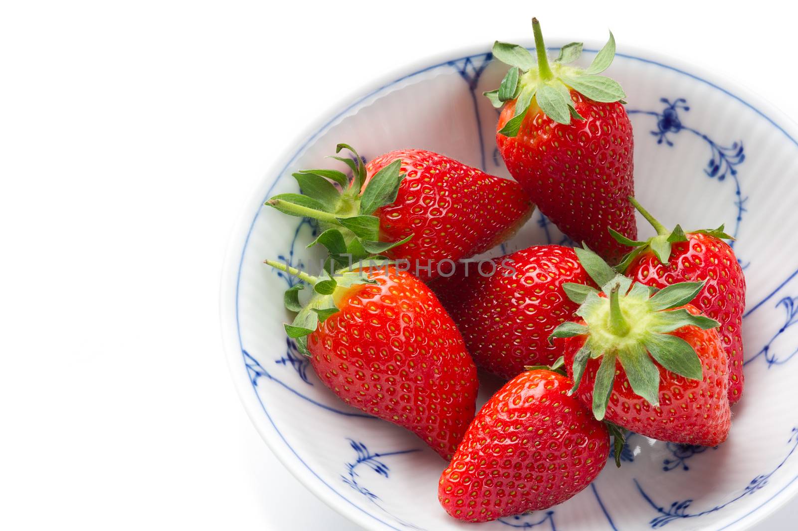 Fresh ripe strawberries, source of antioxidants and vitamin C, in a white bowl with blue decorative pattern, to be served as a healthy snack or dessert, high-angle close-up with copy space on white