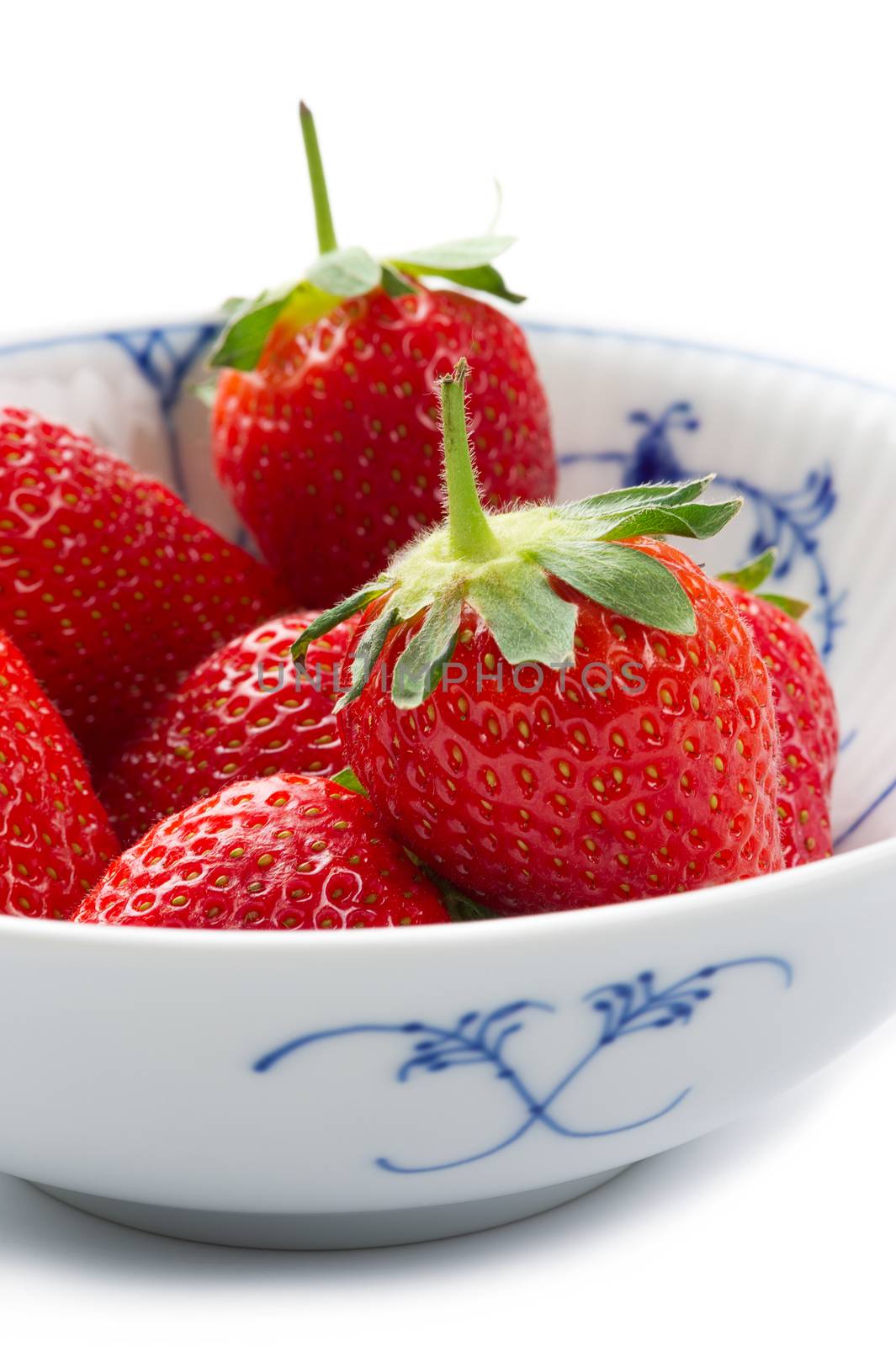 Blue and white porcelain bowl of whole fresh succulent ripe red strawberries with their green stalks attached for a healthy dessert or snack