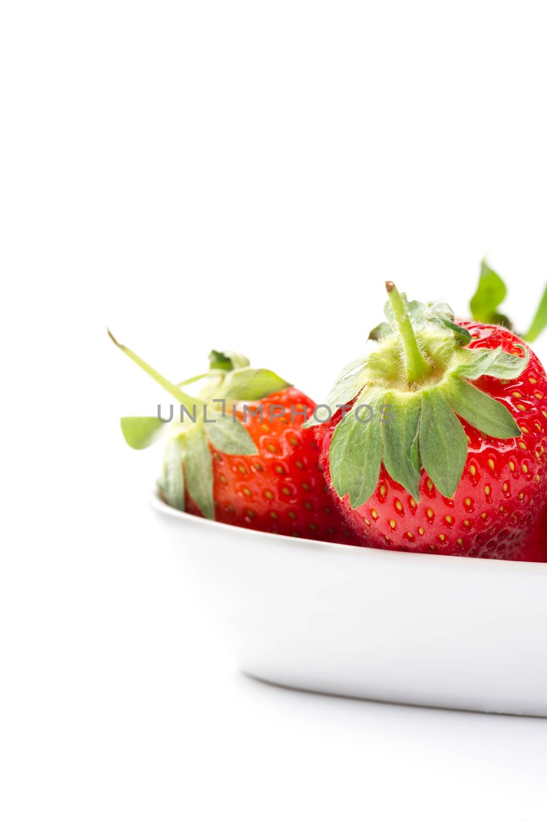 Juicy ripe red whole fresh home grown strawberries in a plain white ceramic bowl with attached green stalks for a healthy finger food snack or cooking and baking ingredient, copyspace on white