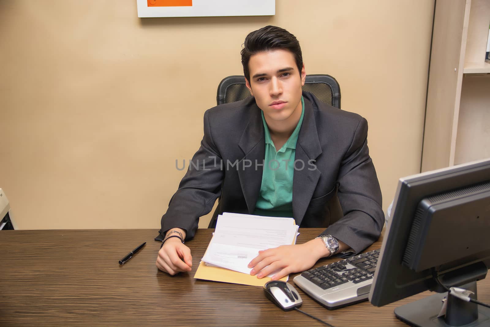 Handsome young businessman sitting at desk in office by artofphoto
