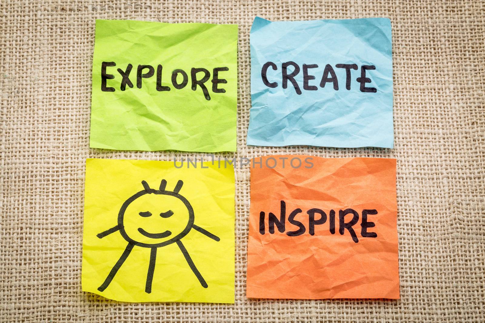 explore, create, inspire and smile reminder on sticky notes against burlap canvas