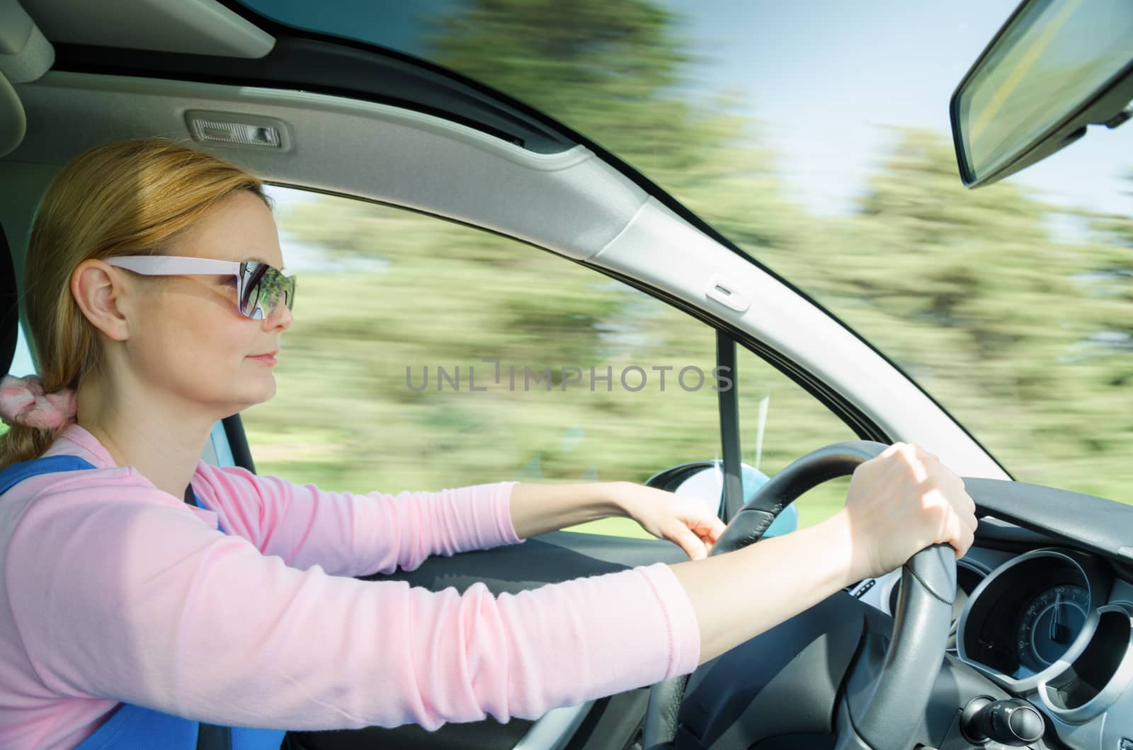 Pretty woman in sunglasses driving fast car with panoramic windscreen. Stock photo with slow shutter on high speed and blurred in motion nature background.